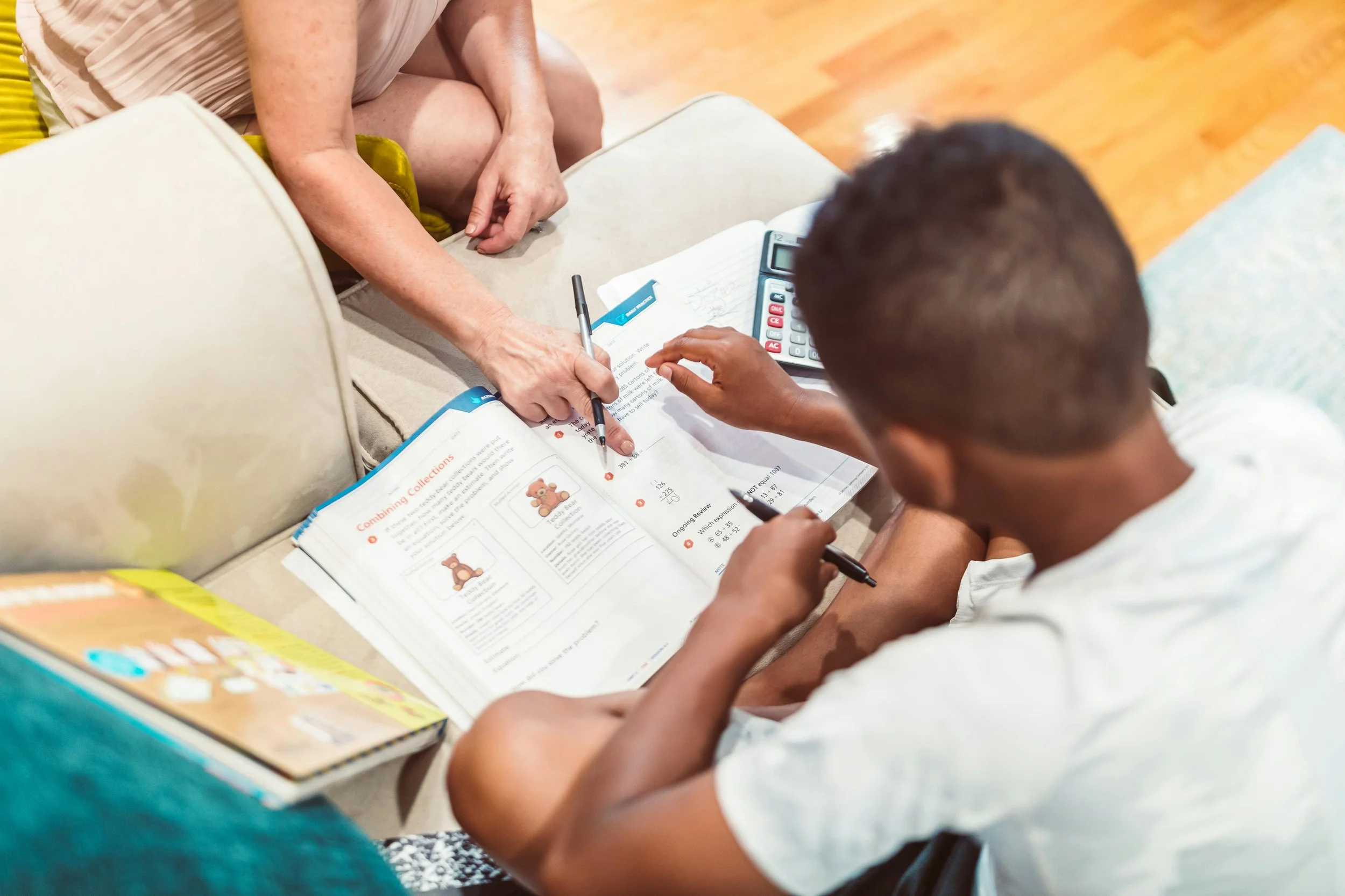 A woman and a young boy studying together at a table, with books, a calculator, and papers.