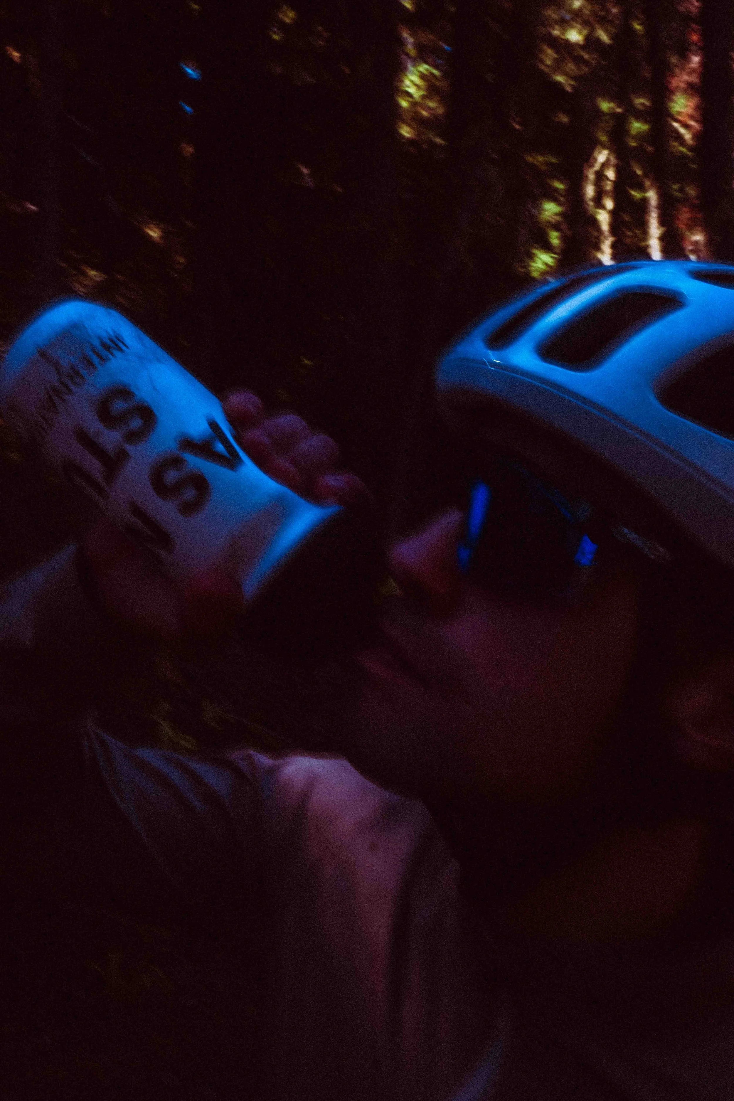 A person holding a white can of spray paint and wearing a bicycle helmet, with trees and evening sky in the background.