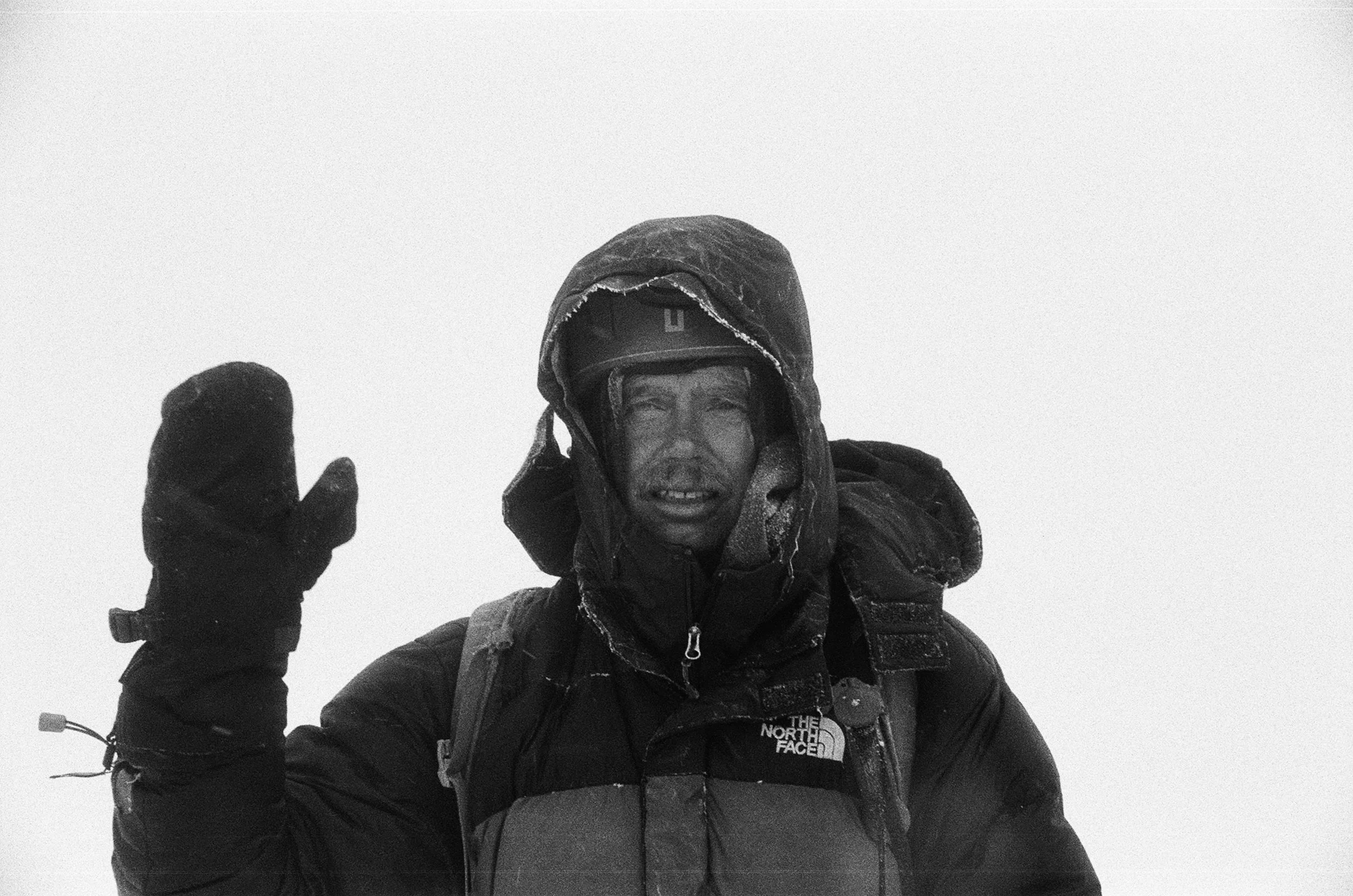 A person in cold weather gear, including a thick jacket and gloves, standing against a foggy or snowy background.
