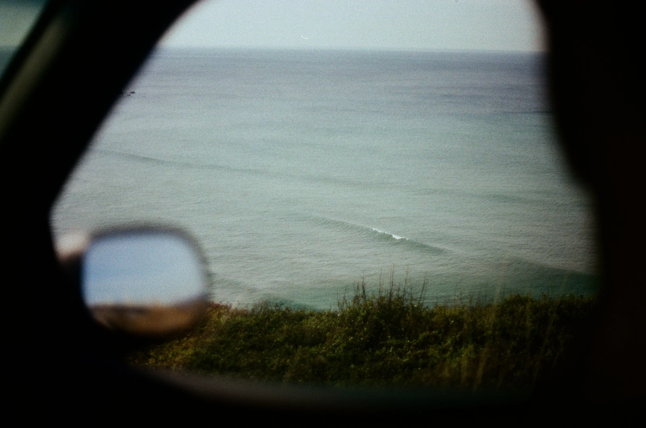 View of the ocean through a binocular lens showing a wave breaking on the water surface, with greenery in the foreground.