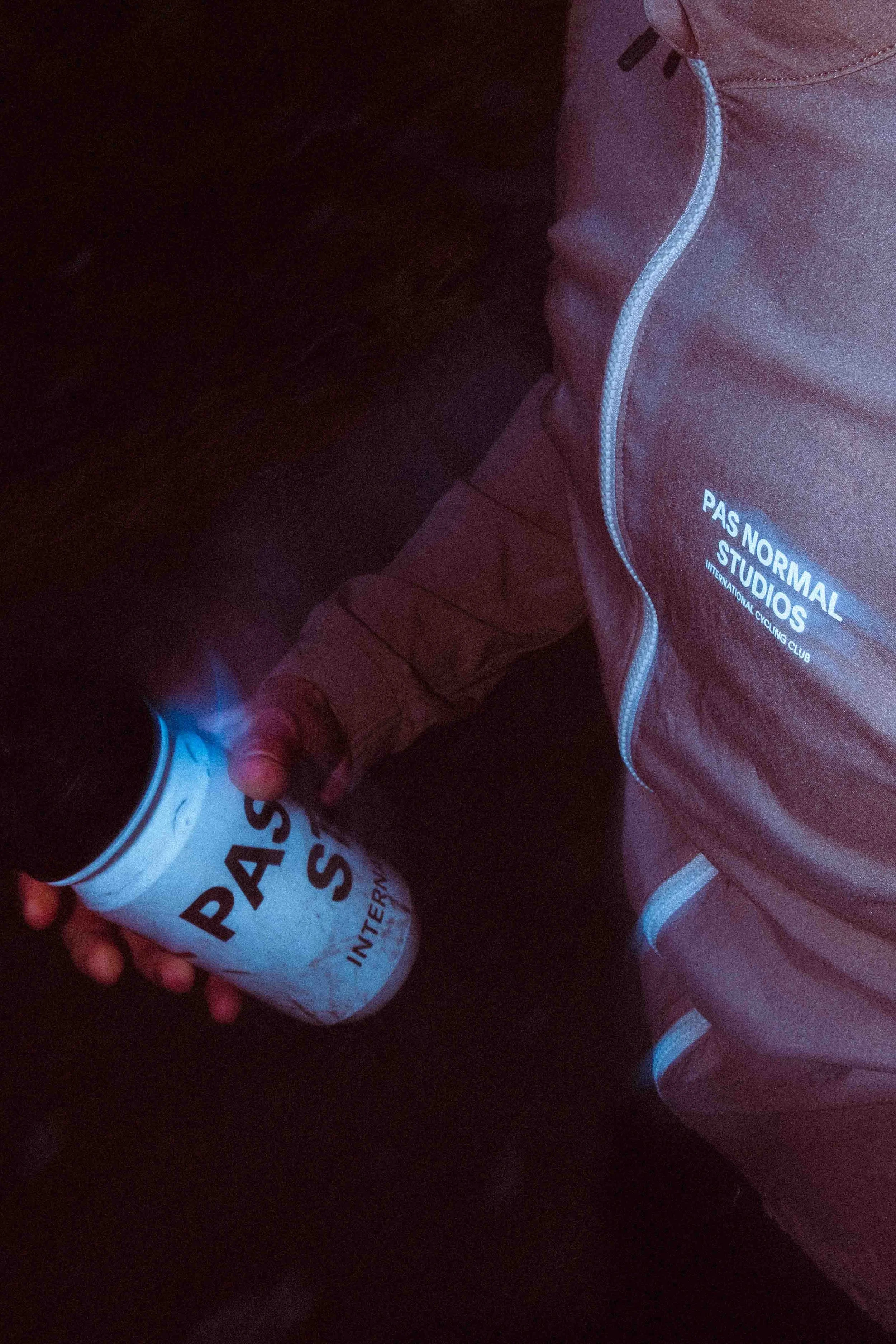Person wearing a PAS NORMAL STUDIOS jacket holding a can of PAS NORMAL STUDIOS International energy drink.