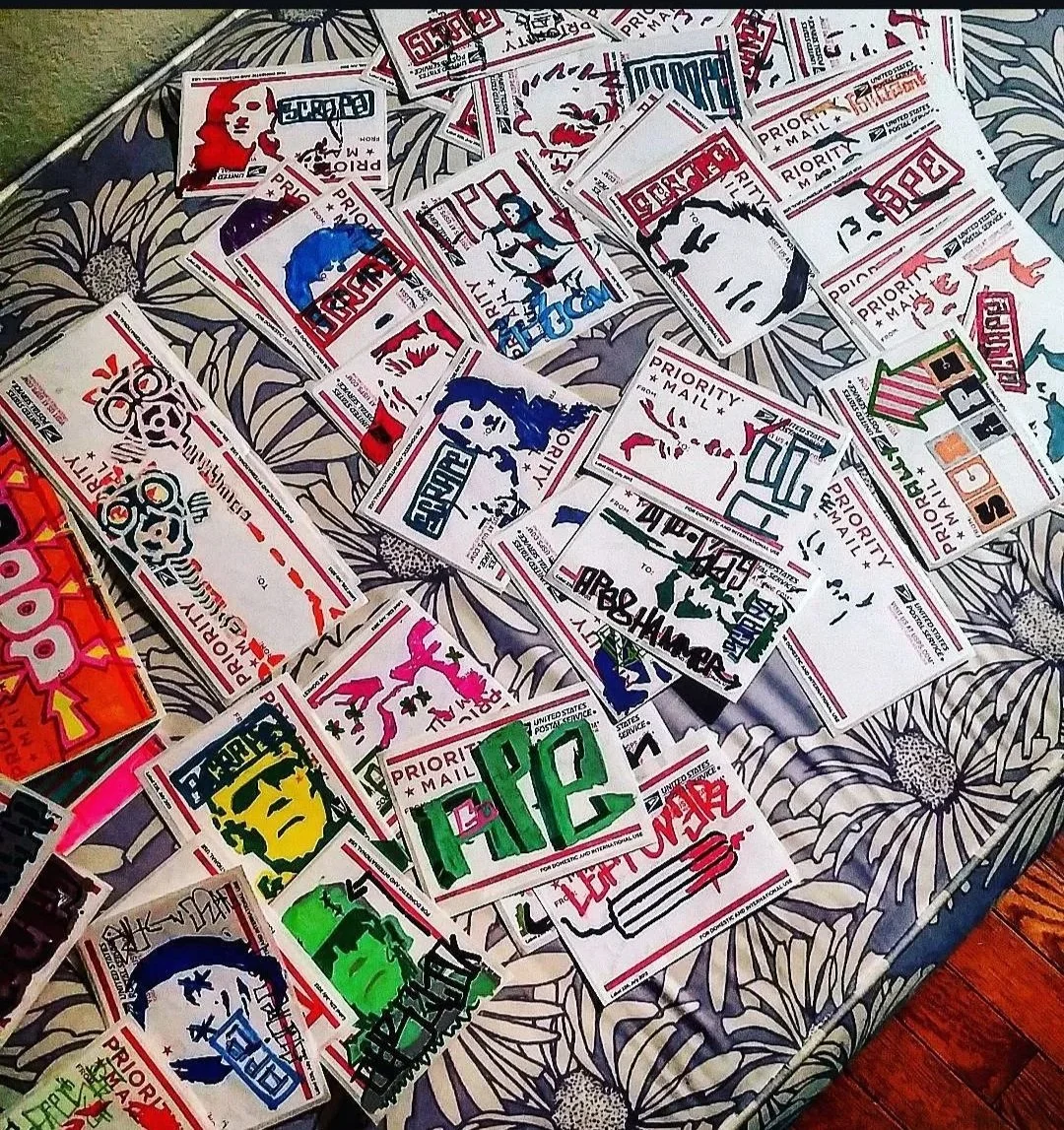 A collection of colorful, hand-drawn postal stickers with portraits and designs, spread out on a floral-patterned surface.
