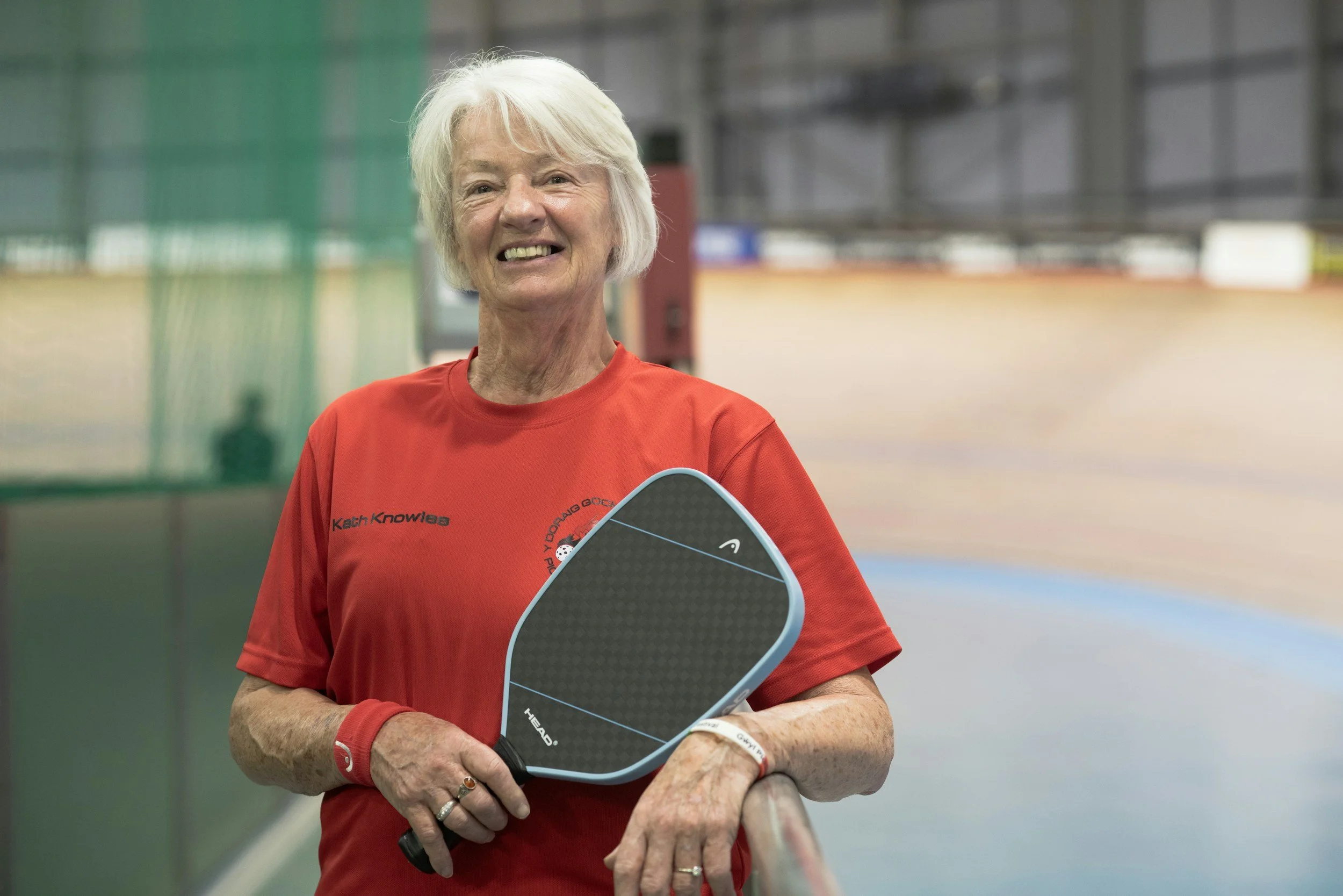 Elderly lady smiling holding a pickleball paddle