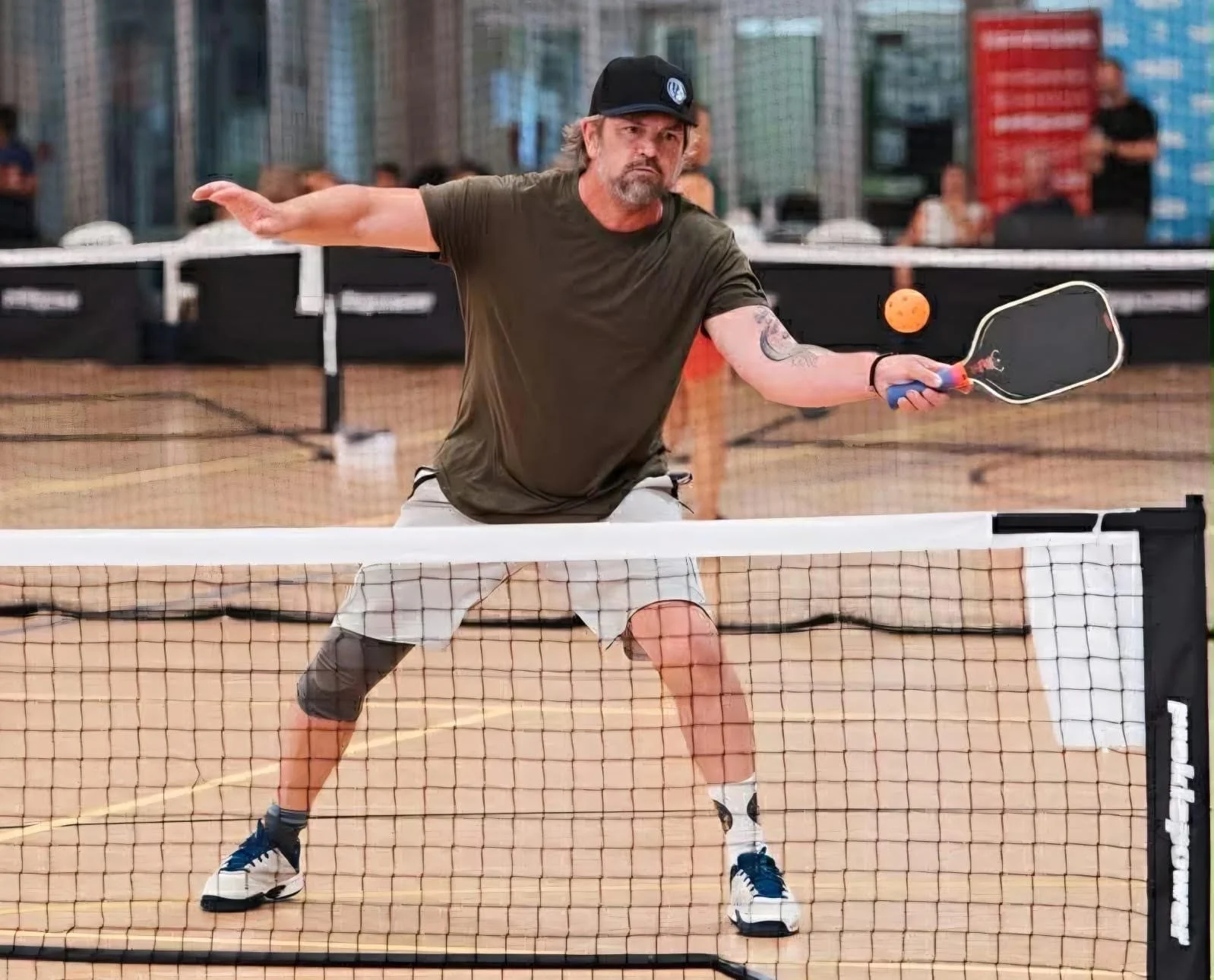 Chris Mooney, founder of Auckland Pickleball Centre, playing pickleball, hitting an orange ball with a black paddle, on an indoor court.
