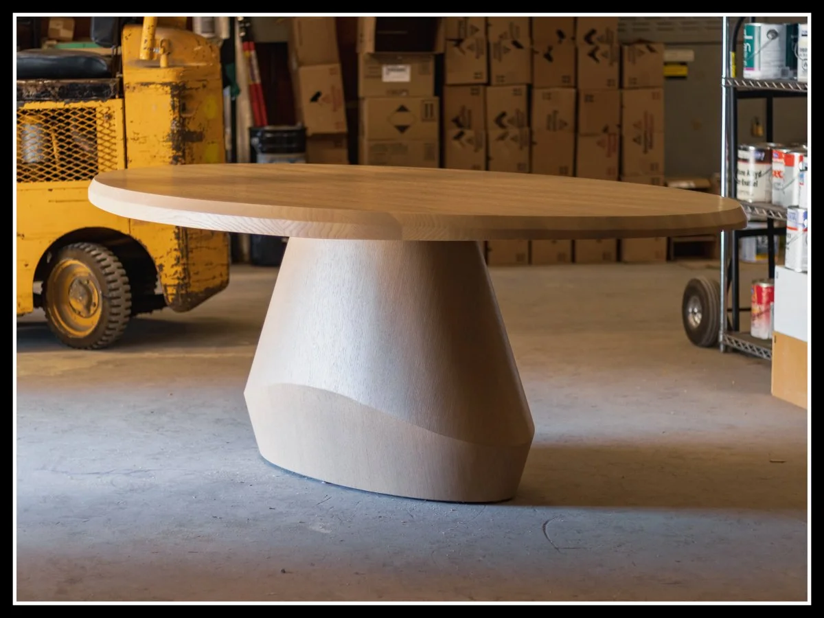Red oak table lit by diffused daylight from an open overhead door, with soft floor bounce and a forklift in the background adding industrial contrast.