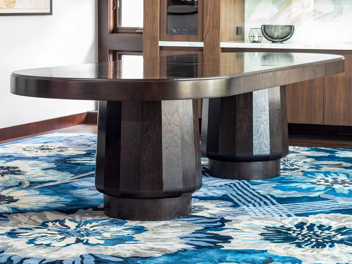 A black walnut dining table with thick, rounded pedestal legs
