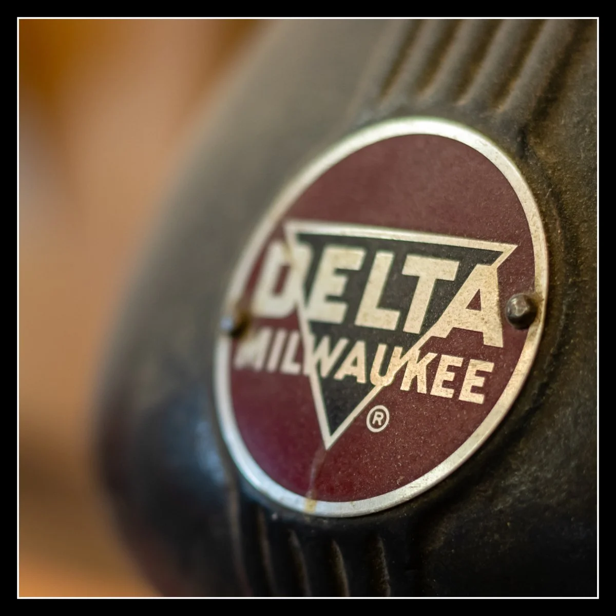 Close-up of a vintage Milwaukee Delta tool logo with a red and black background and metallic border.