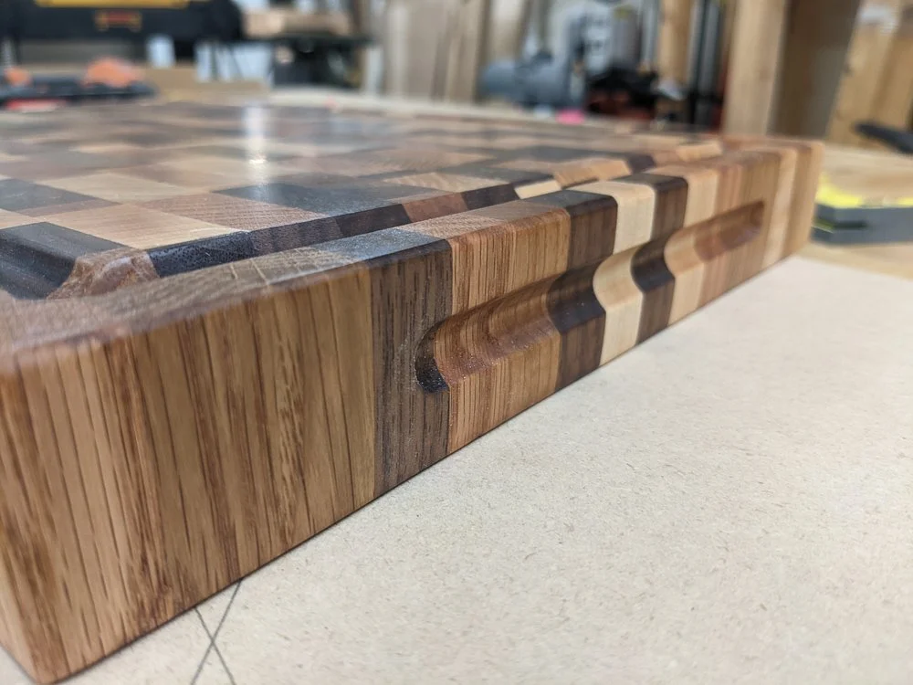 End‑grain cutting board showing carved finger grip and juice groove, made from mixed hardwoods.