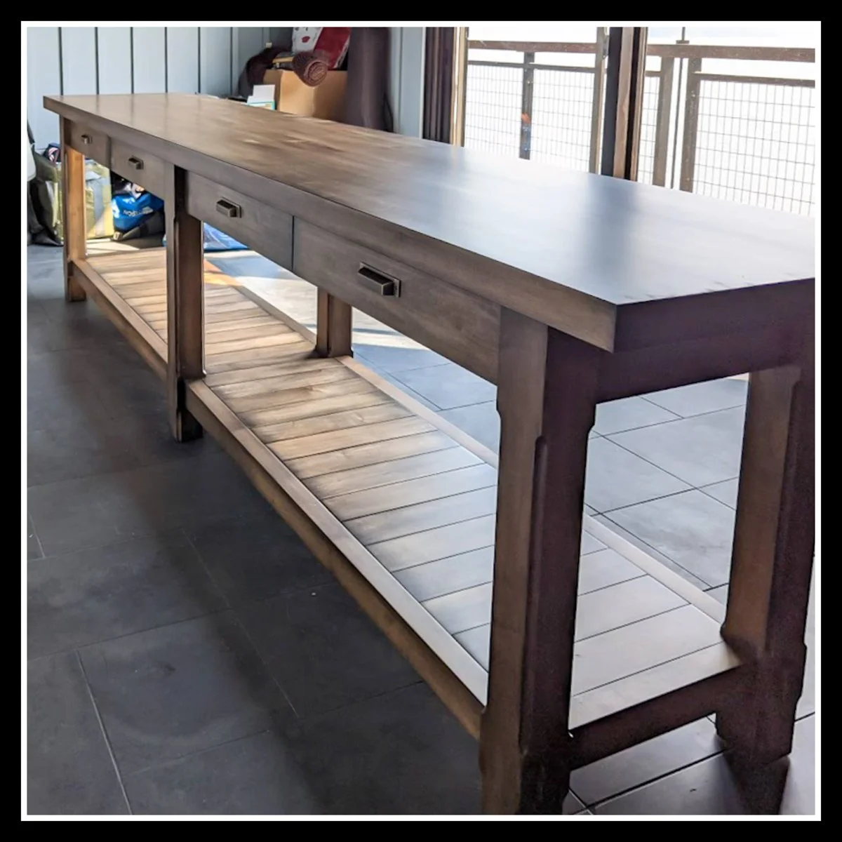 Solid maple laundry table with stained finish, 2K poly clear coat, four drawers, slatted lower shelf, and sturdy legs, positioned indoors with natural light on the wood grain.