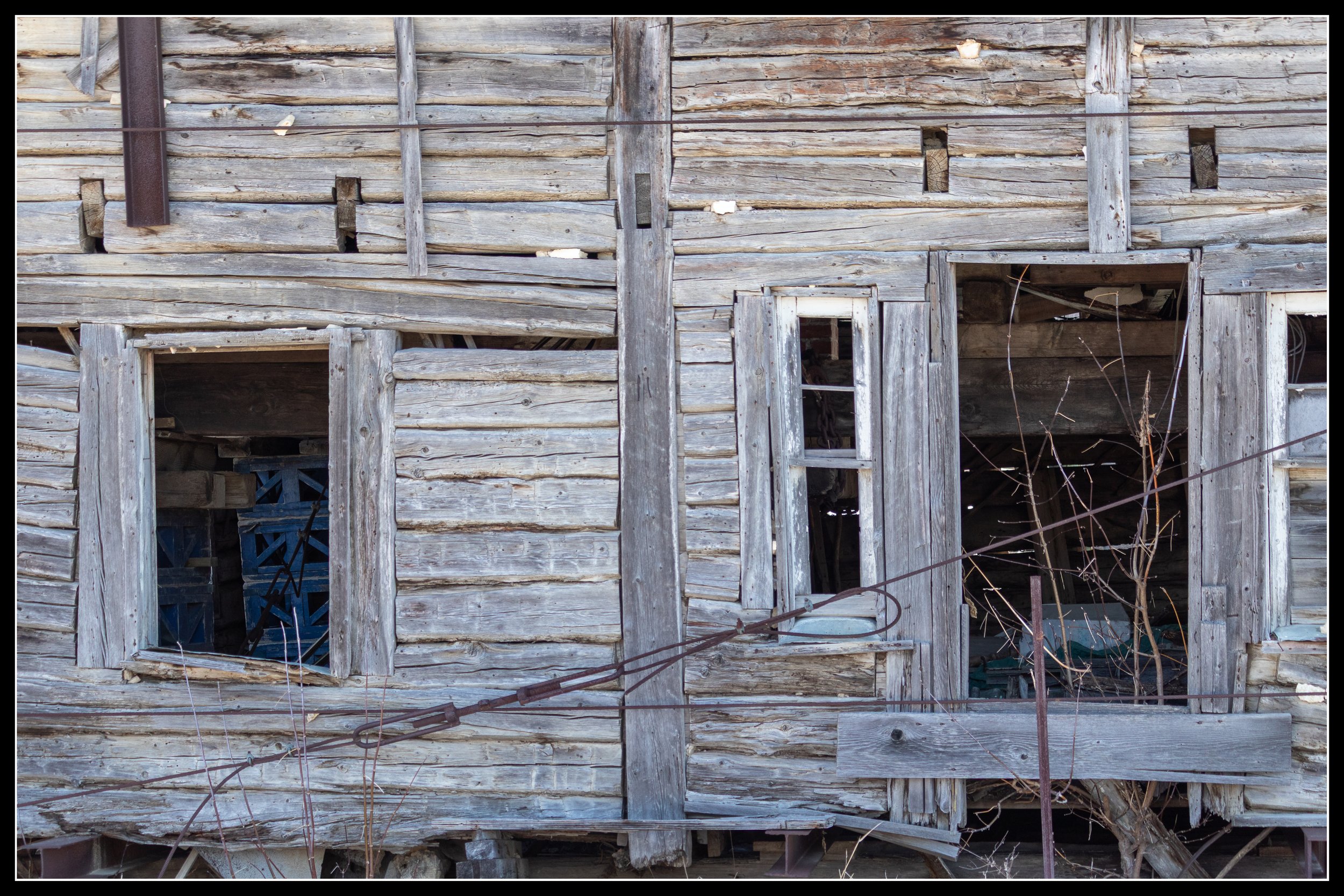 Weathered 1850s bur oak post‑and‑frame house with missing siding and exposed beams, representing Henderson House, the oldest surviving settler‑era home in Manitoba.