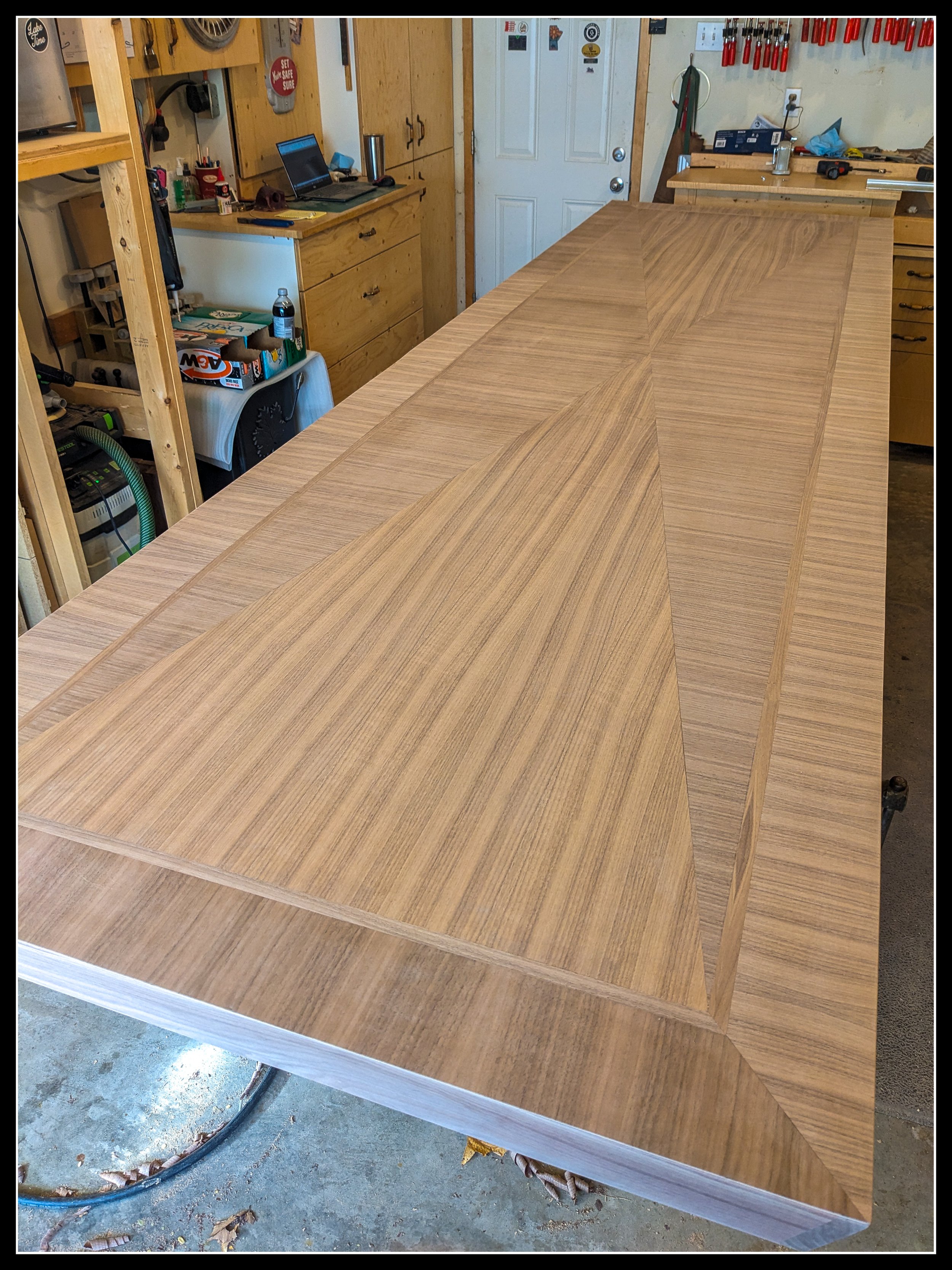 12‑foot walnut table with rift‑cut geometric veneer pattern on a workbench, showing precise grain alignment, triangular layout, and clean symmetry before finishing.