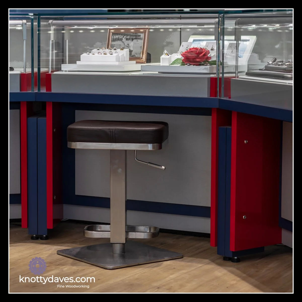 Jewellery store cabinetry with red, blue, and grey panels, ½‑inch thick glass display top, custom lighting, and commercial‑grade construction.