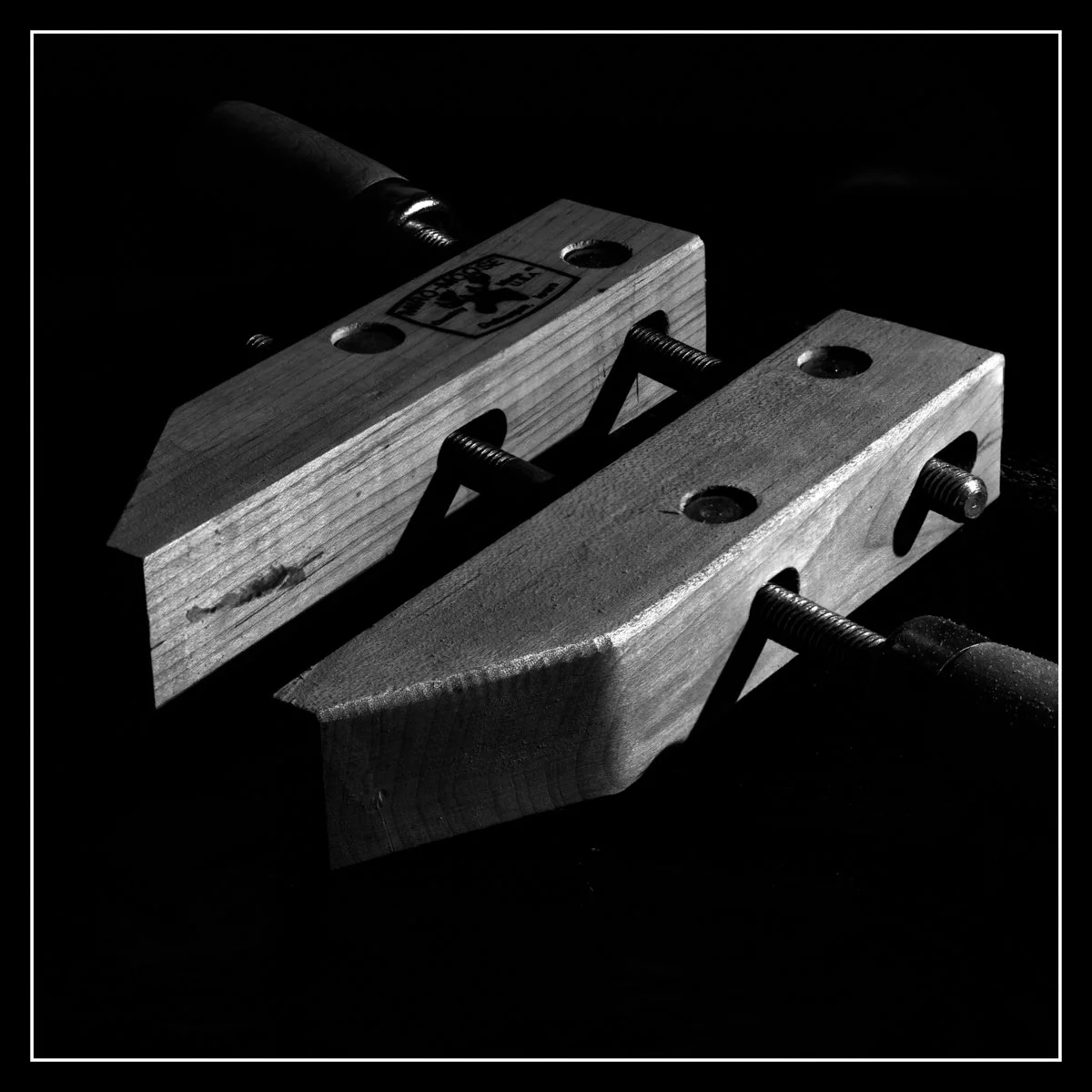Wooden handscrew clamp photographed with dramatic shop lighting, highlighting the texture of the wood and metal hardware as a symbol of perspective during recovery.