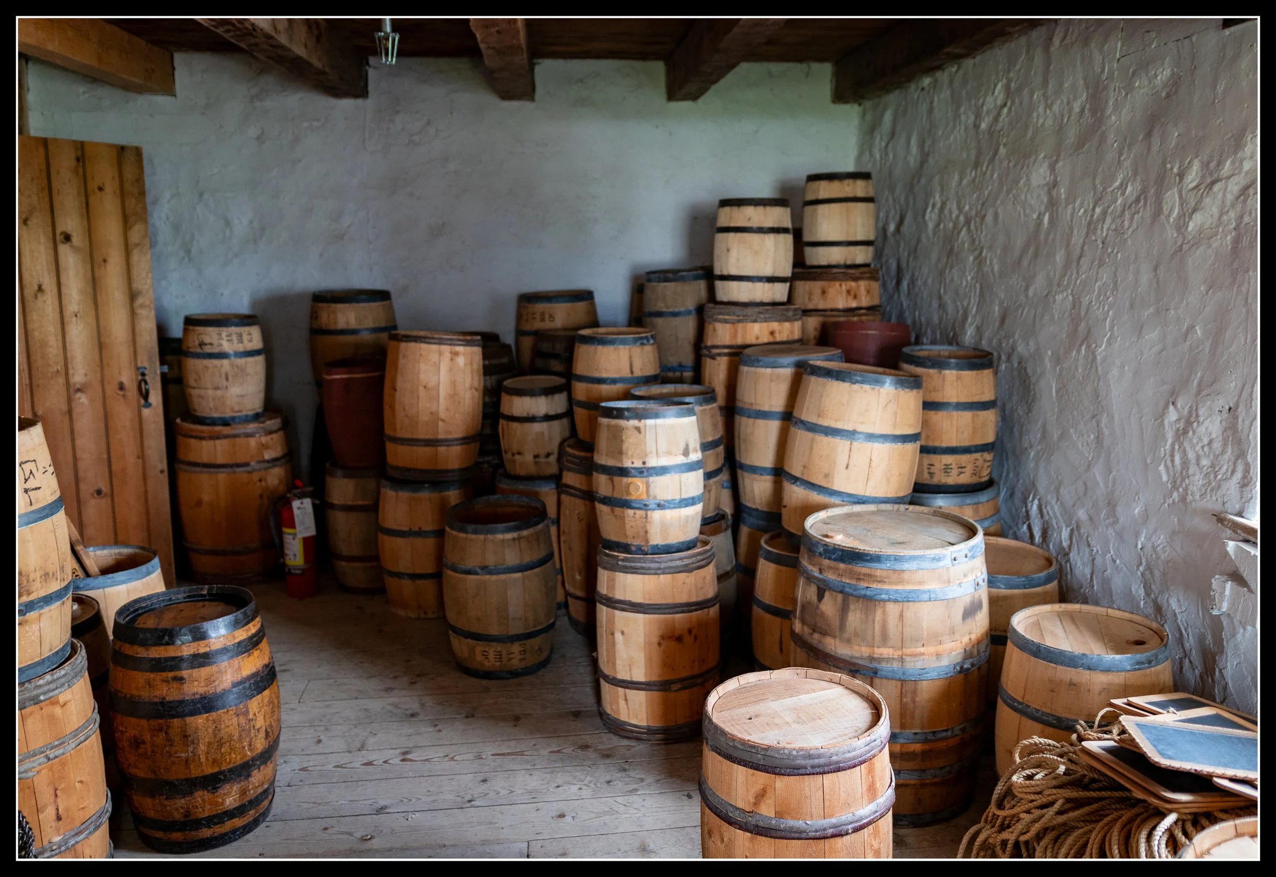 White oak barrels stacked in a heritage-style room with plaster walls and timber beams, illustrating the durability, water‑tightness, and slow‑grown density that distinguish white oak from red oak in woodworking and Prairie home history.