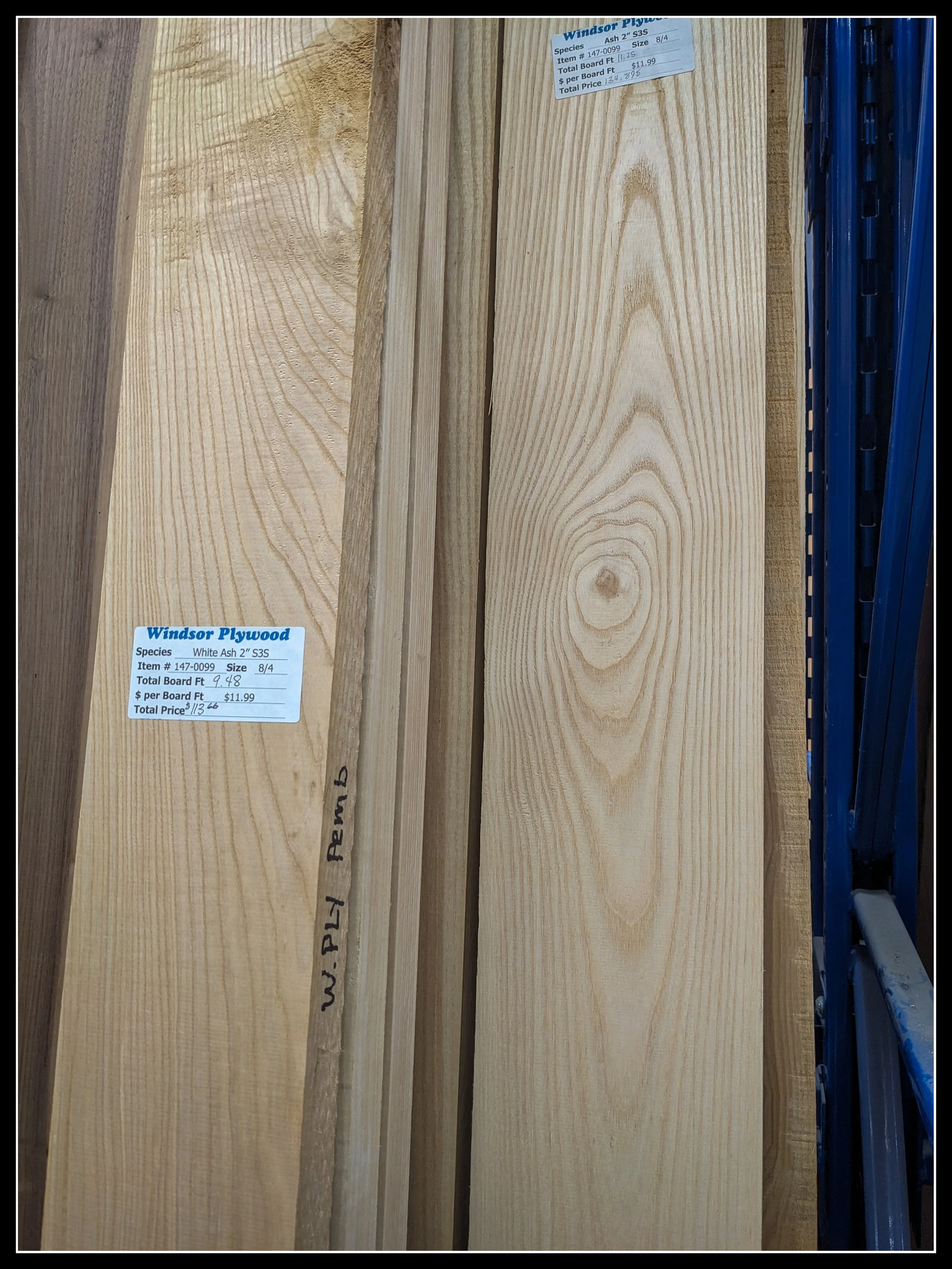 White ash hardwood boards displayed vertically at a lumber yard, showing grain and product labels.