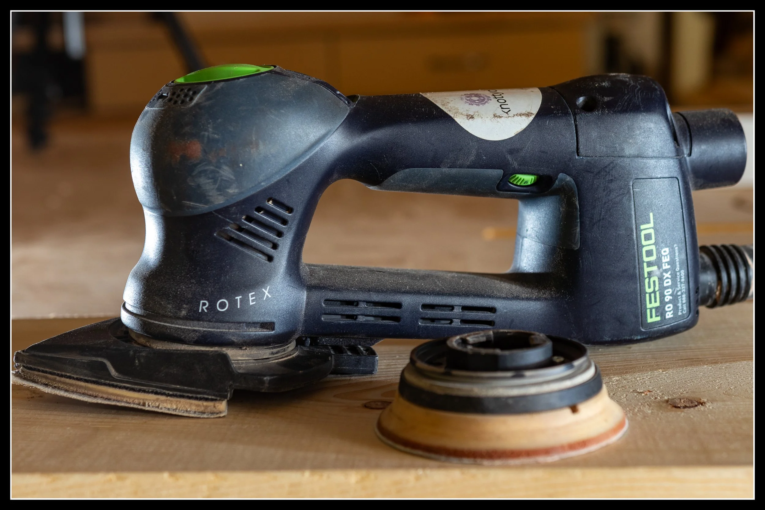 Festool RO 90 configured with a triangular detail‑sander pad, with the optional orbital pad resting behind it on the bench.
