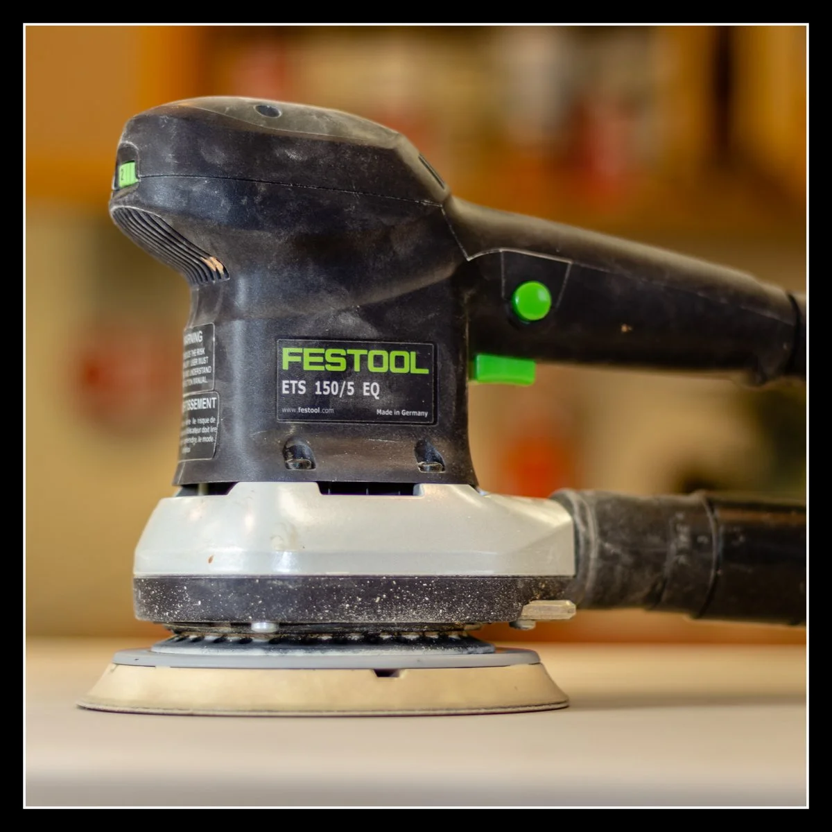 Festool ETS 150/5 orbital sander with dust‑extraction hose attached, sitting in a woodworking shop