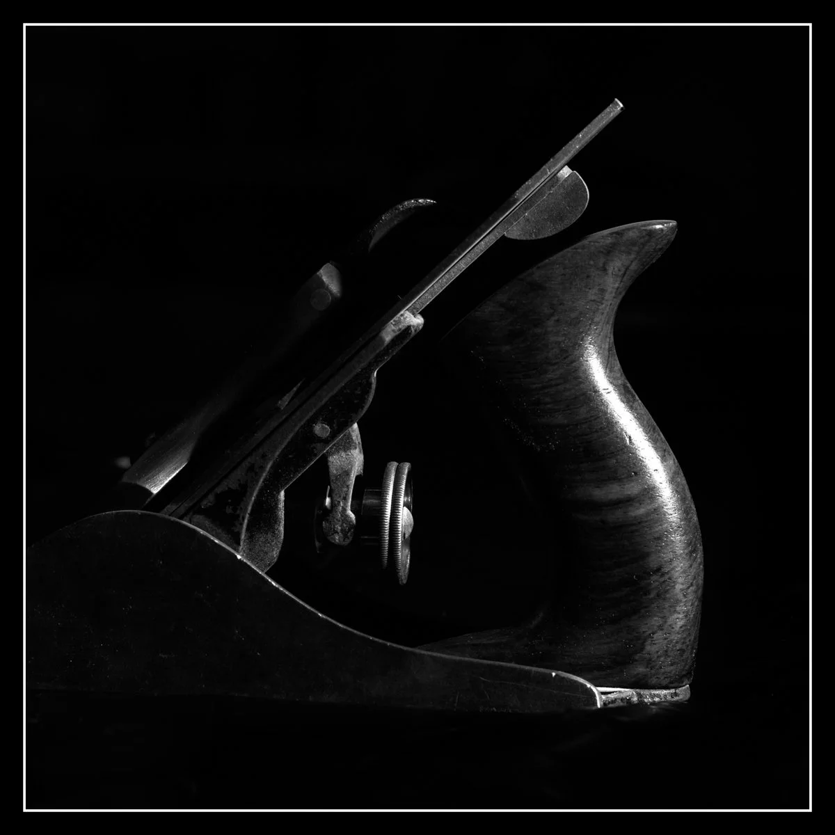 Hand plane photographed with a single backlight flash on a black background, highlighting the edges and tool contours.