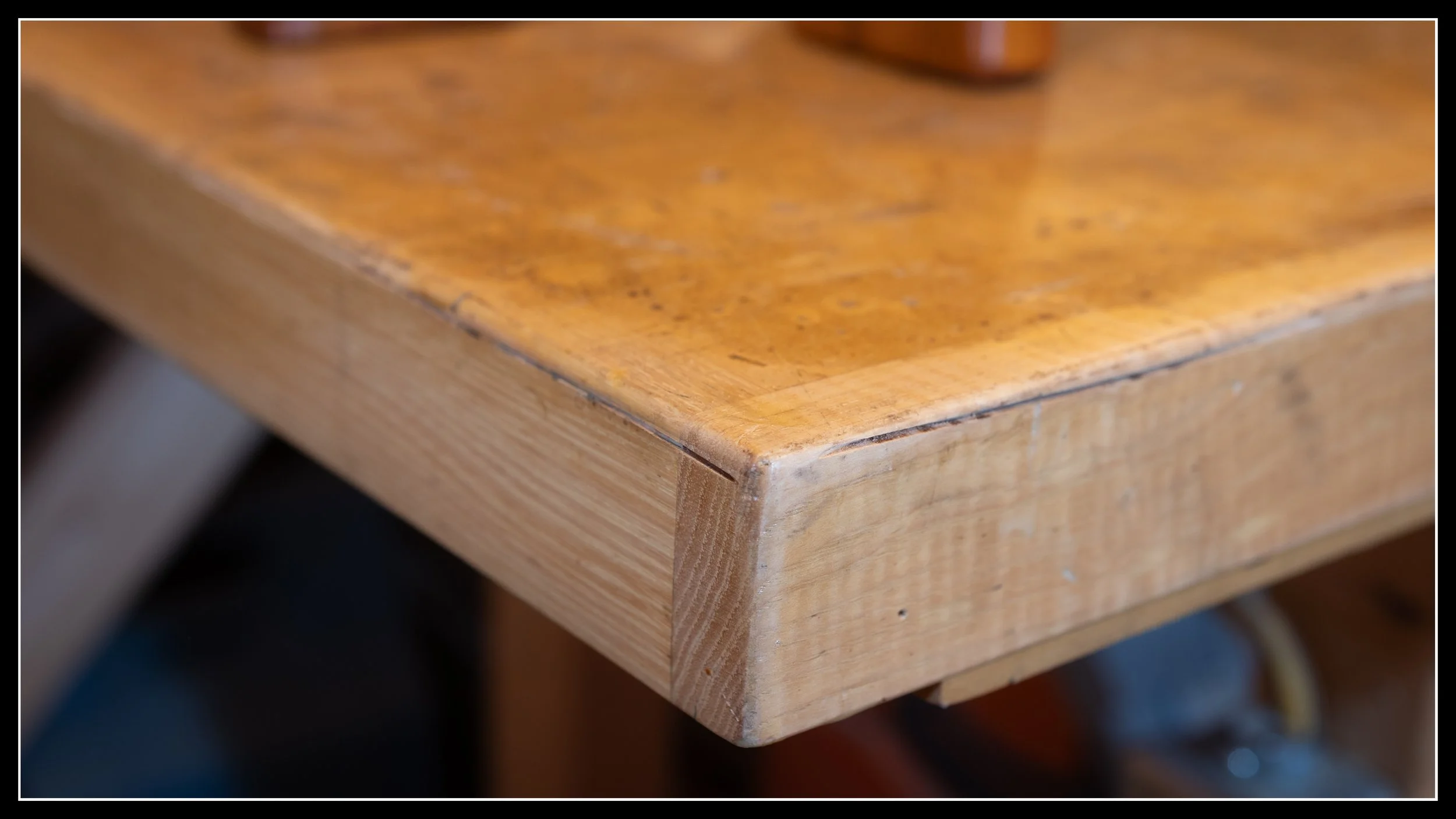 Close‑up of a hickory workbench edge showing dense grain and heavy wear from years of woodworking, highlighting hickory’s long‑term durability and impact resistance.