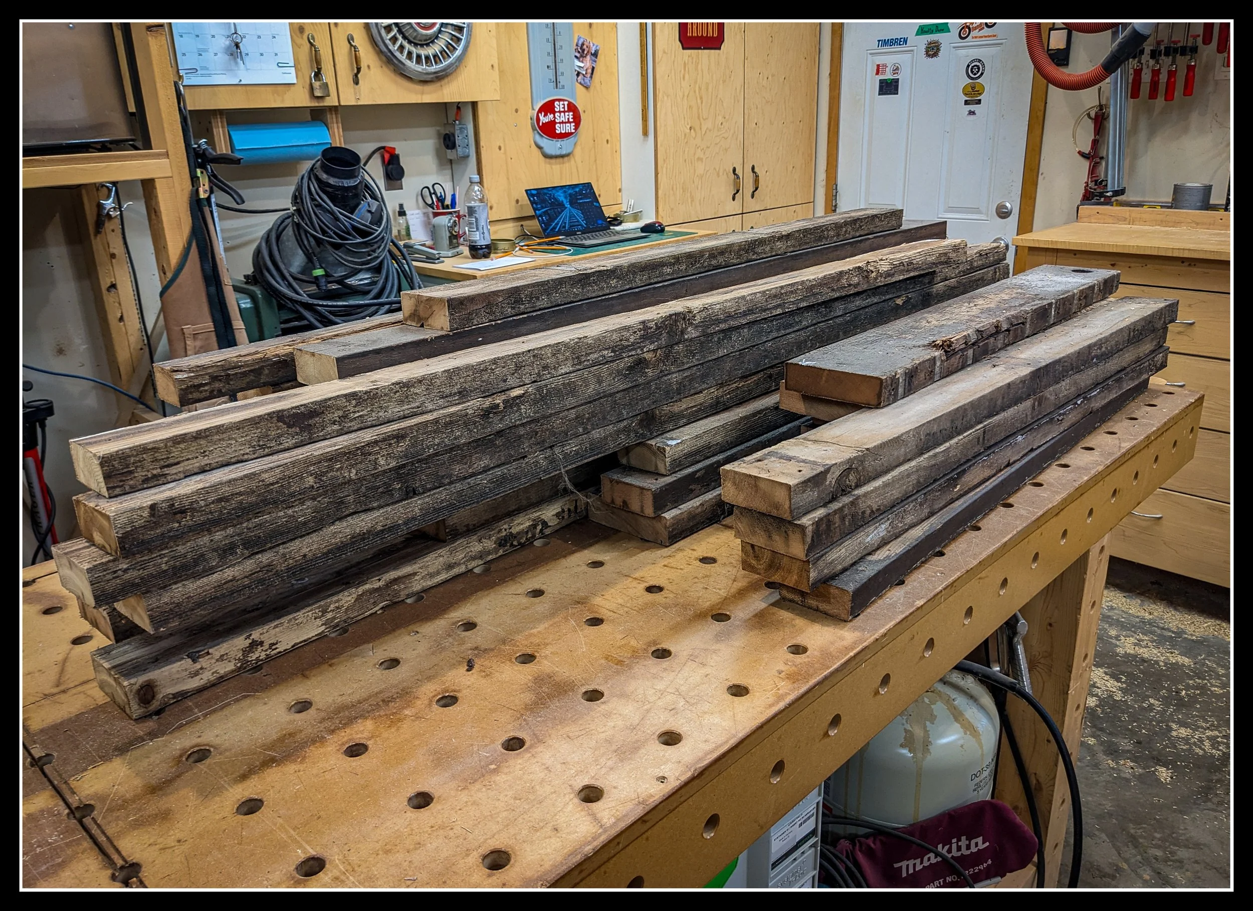 Stack of dried reclaimed cedar boards in a woodworking shop, ready for milling after fifty years of weathering.
