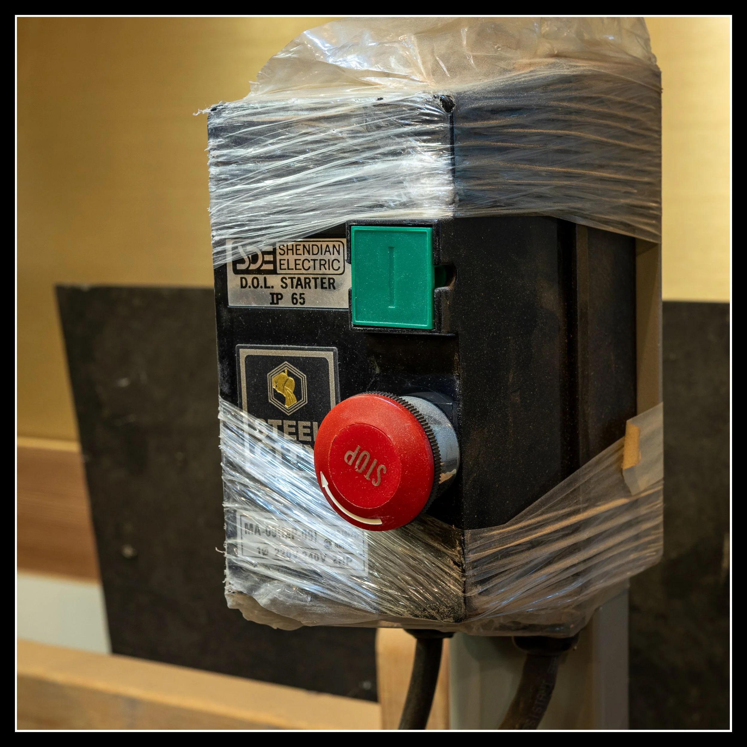 Close‑up of Steel City jointer power switch with red STOP button and green START button, showing minor impact mark from red oak; evidence of a jointer used in an active woodworking shop.