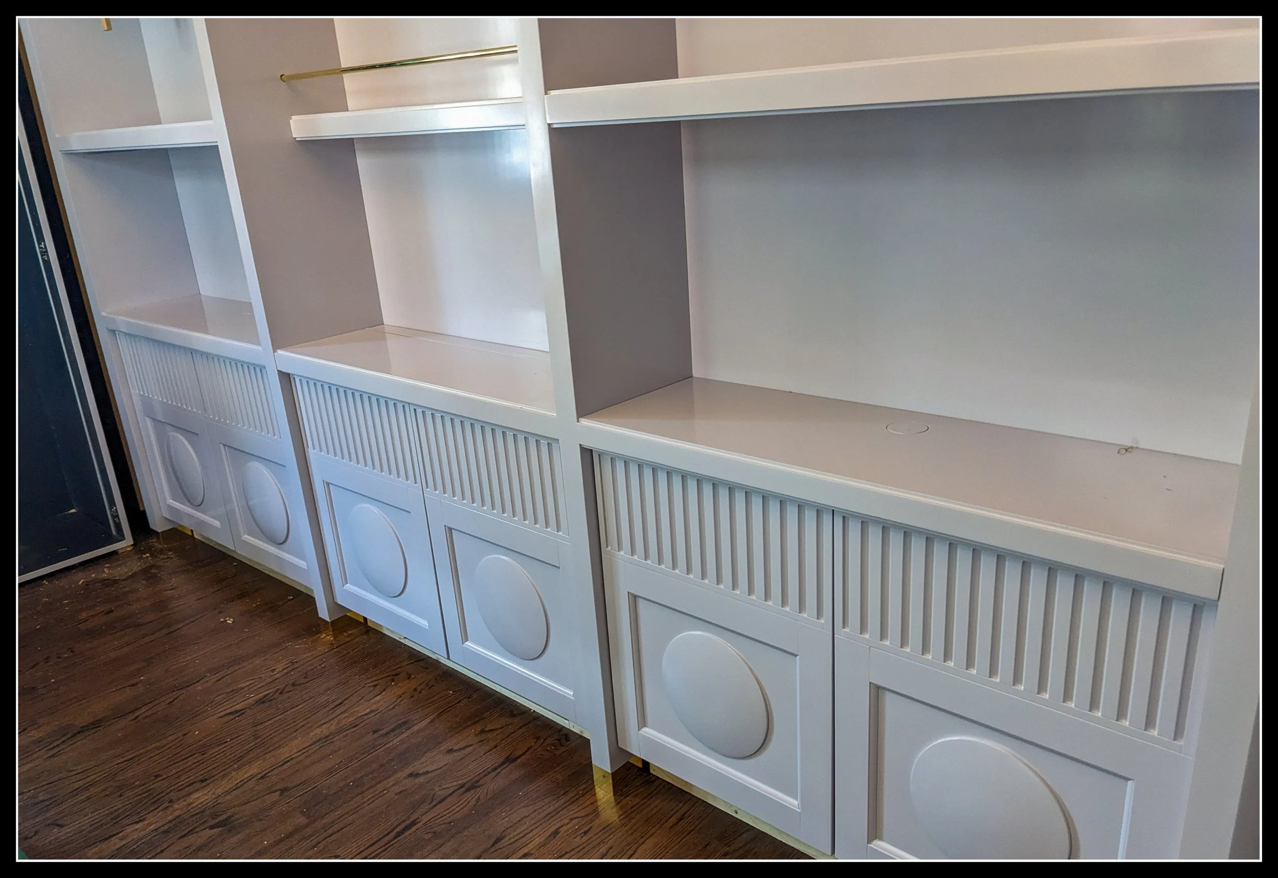 Gloss‑grey built‑in cabinetry with lathe‑turned raised panels, fluted doors, brass accents, and open shelving in a high‑skill architectural room.