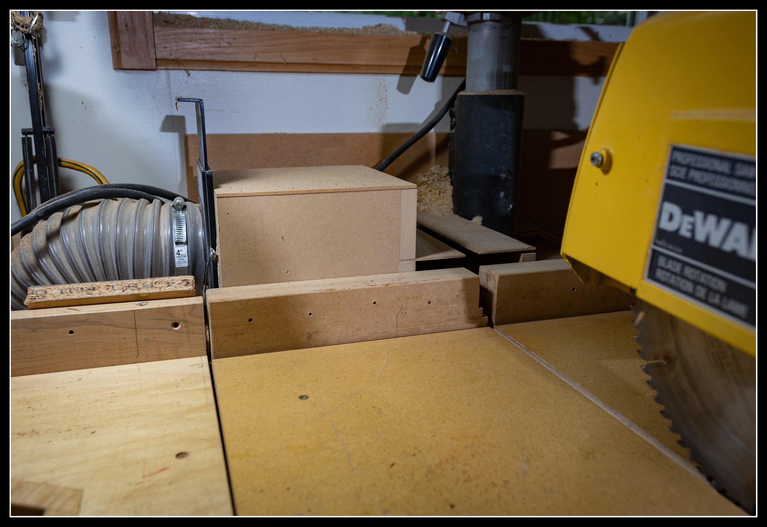 Radial arm saw dust‑collection setup showing dust thrown backward into the fence and captured by the collection port during cross‑cuts.