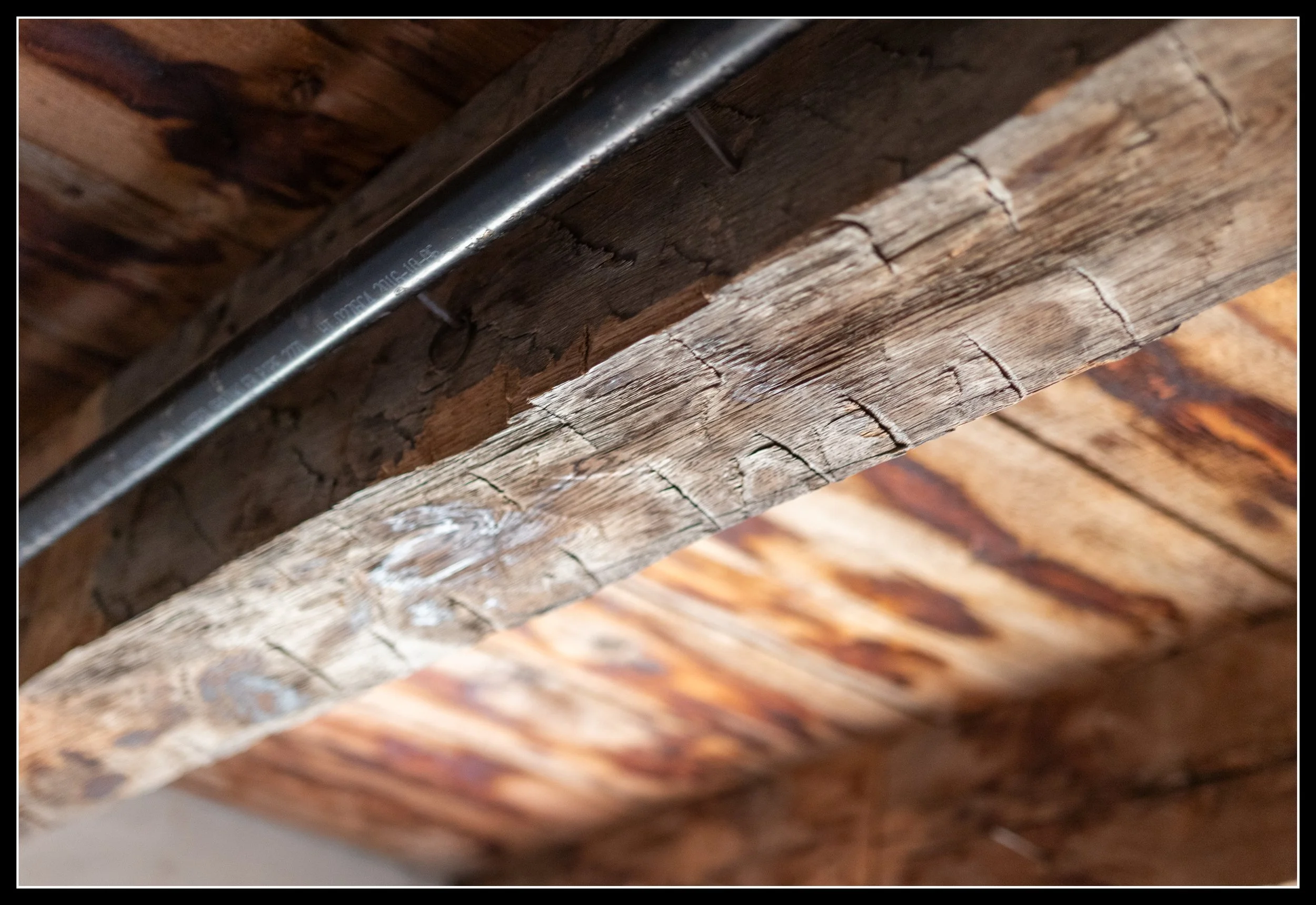 Hand‑hewn pioneer‑era beam with visible adz marks inside Lower Fort Garry, supporting a ceiling with a modern pipe running above it.