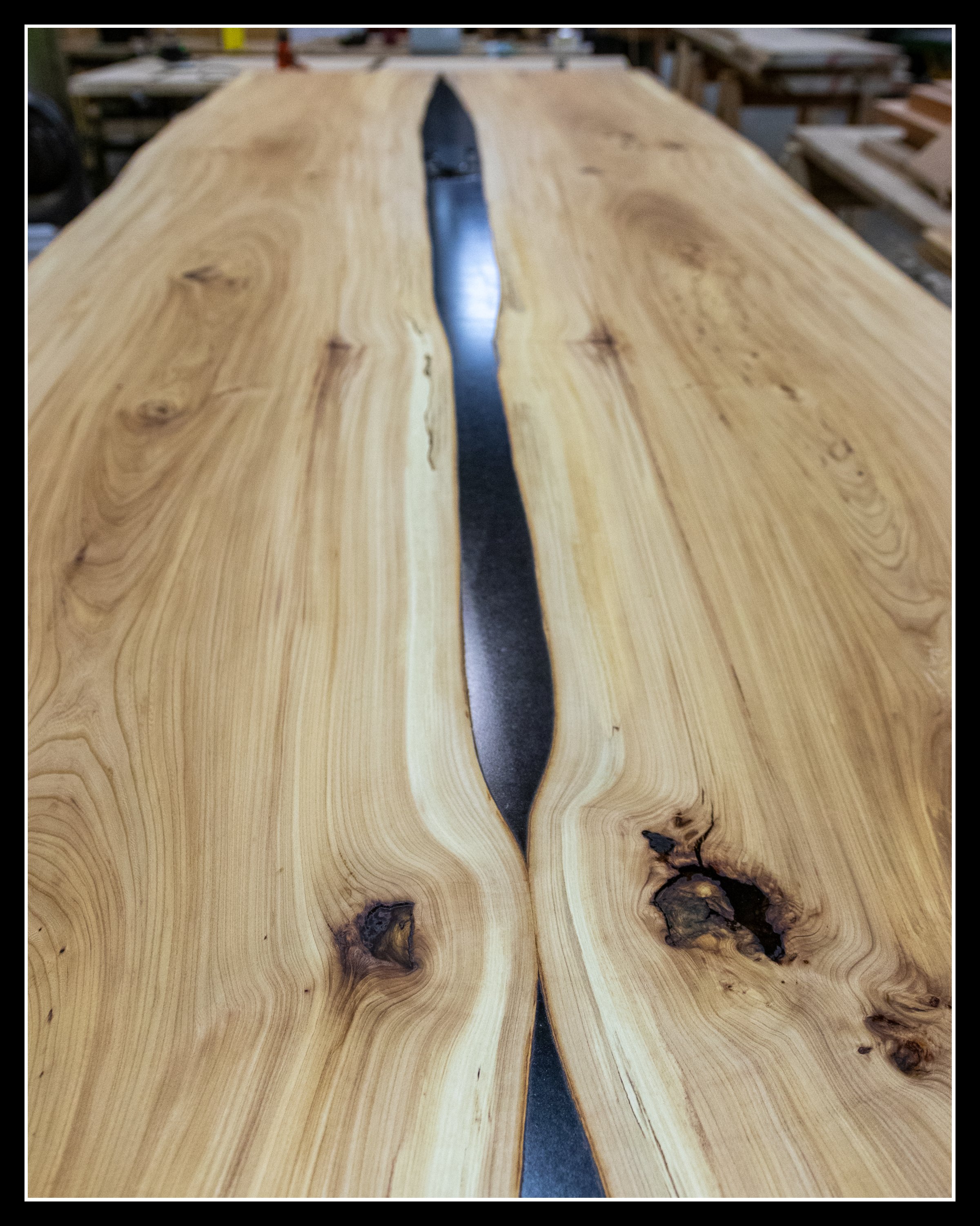 Bookmatched elm slabs joined with dark epoxy, freshly sanded to reveal wavy grain and natural colour variation.