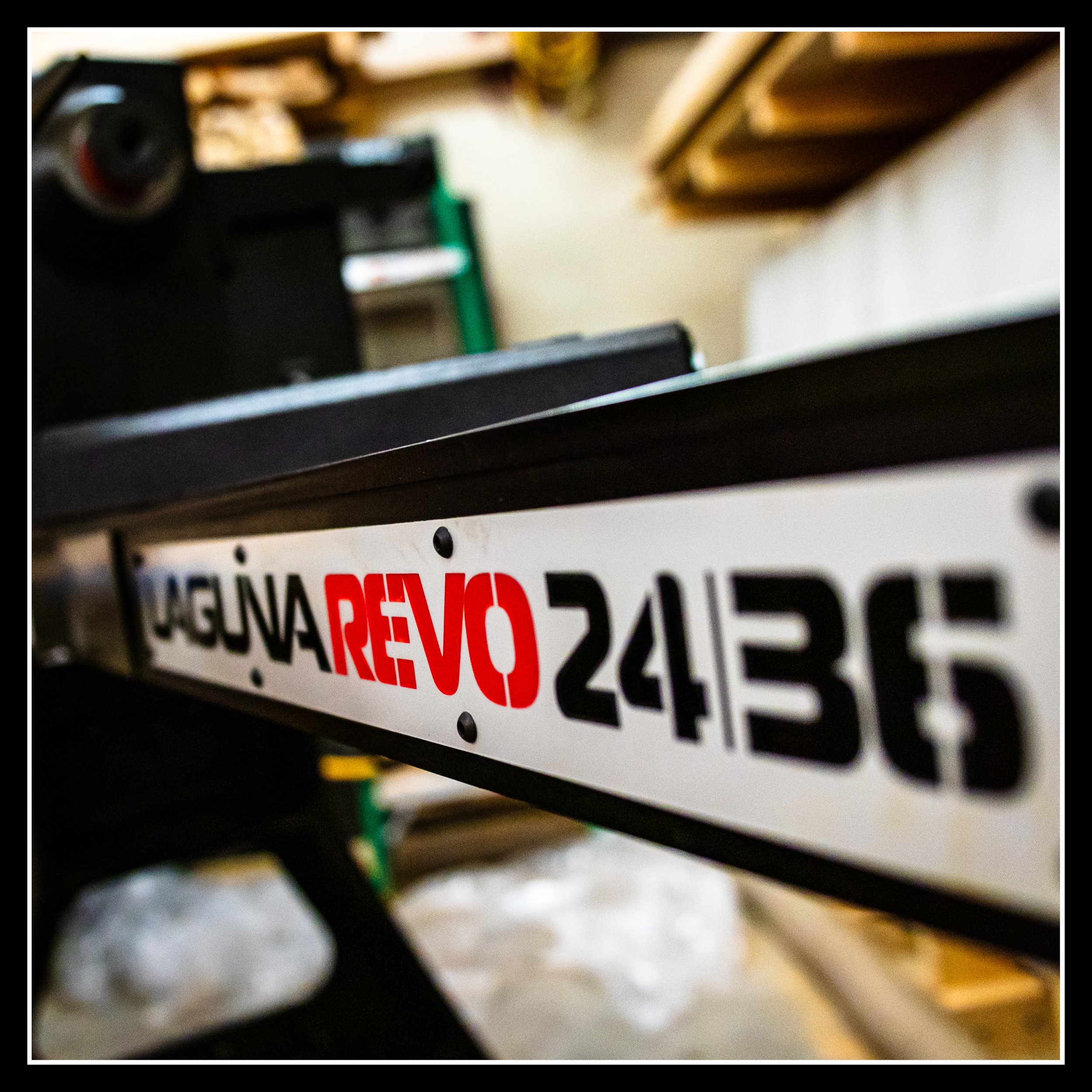 Close‑up of the Laguna Revo 24/36 woodworking lathe name plate on the main beam, showing the raised lettering, brushed metal surface, and workshop background that reflects the machine’s size, power, and presence in the shop.