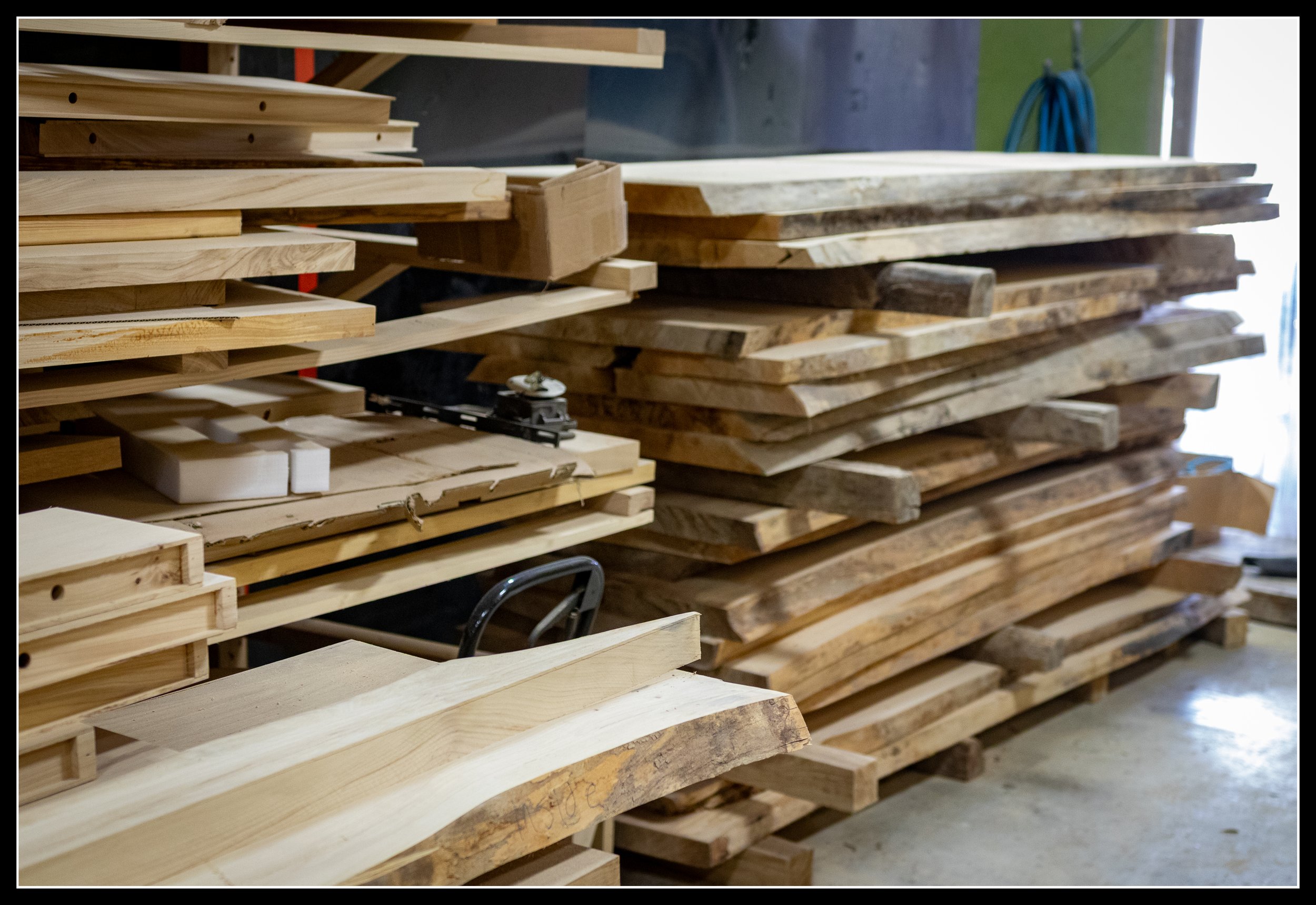 A stack of kiln‑dried elm boards in a modern workshop, illustrating how easily wood can be purchased and transported today compared to the demanding hand‑harvested timber supply of the 19th‑century fur‑trade era.