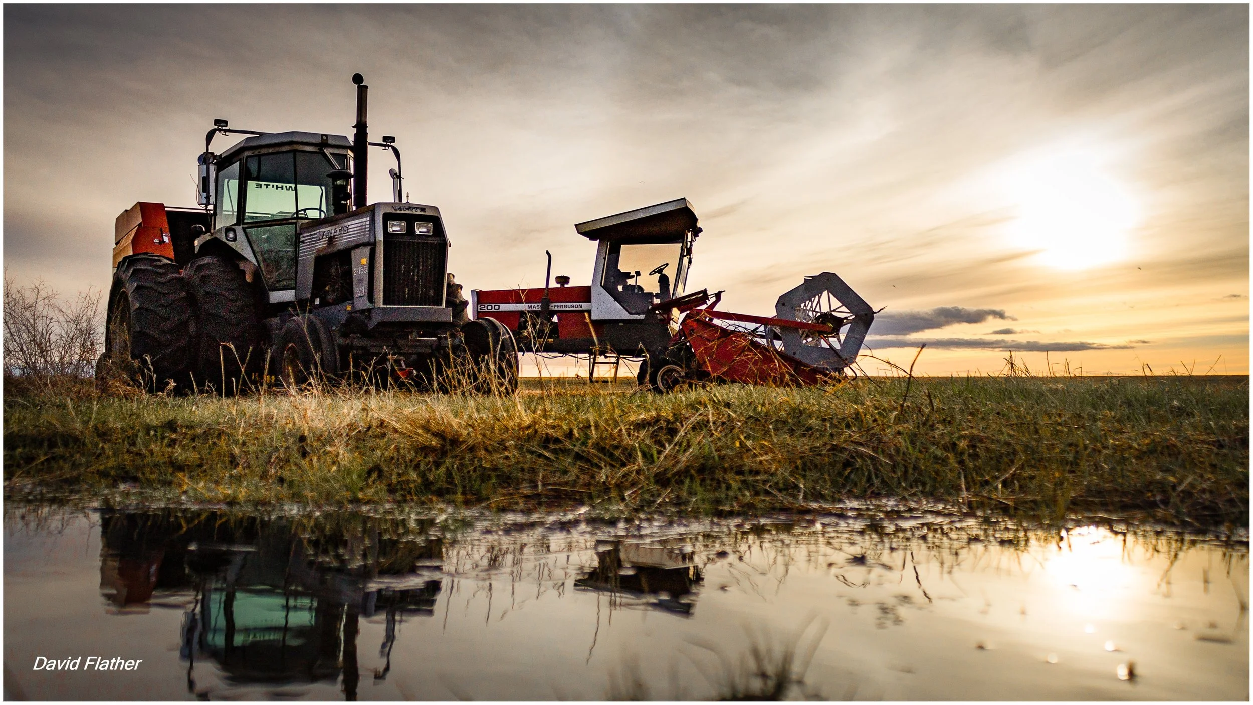 Tractors in a drying spring field after rain, reflecting warm sunlight in a puddle — a moment of quiet storytelling captured through photography.