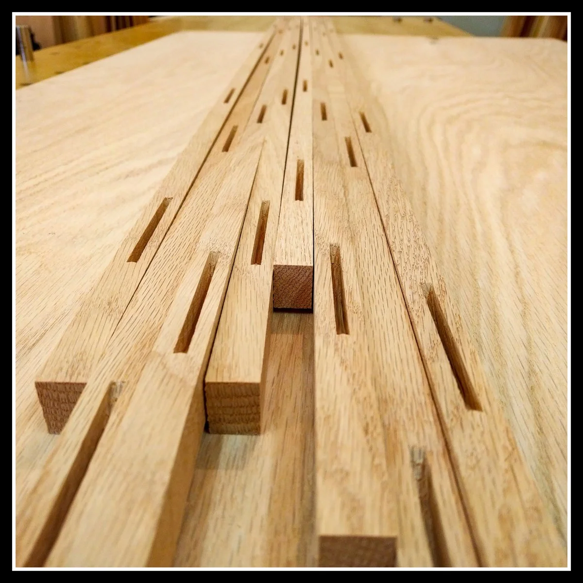 Red oak parts with clean mortises laid out on a red‑oak‑veneered panel, prepared for assembly in a woodworking shop.
