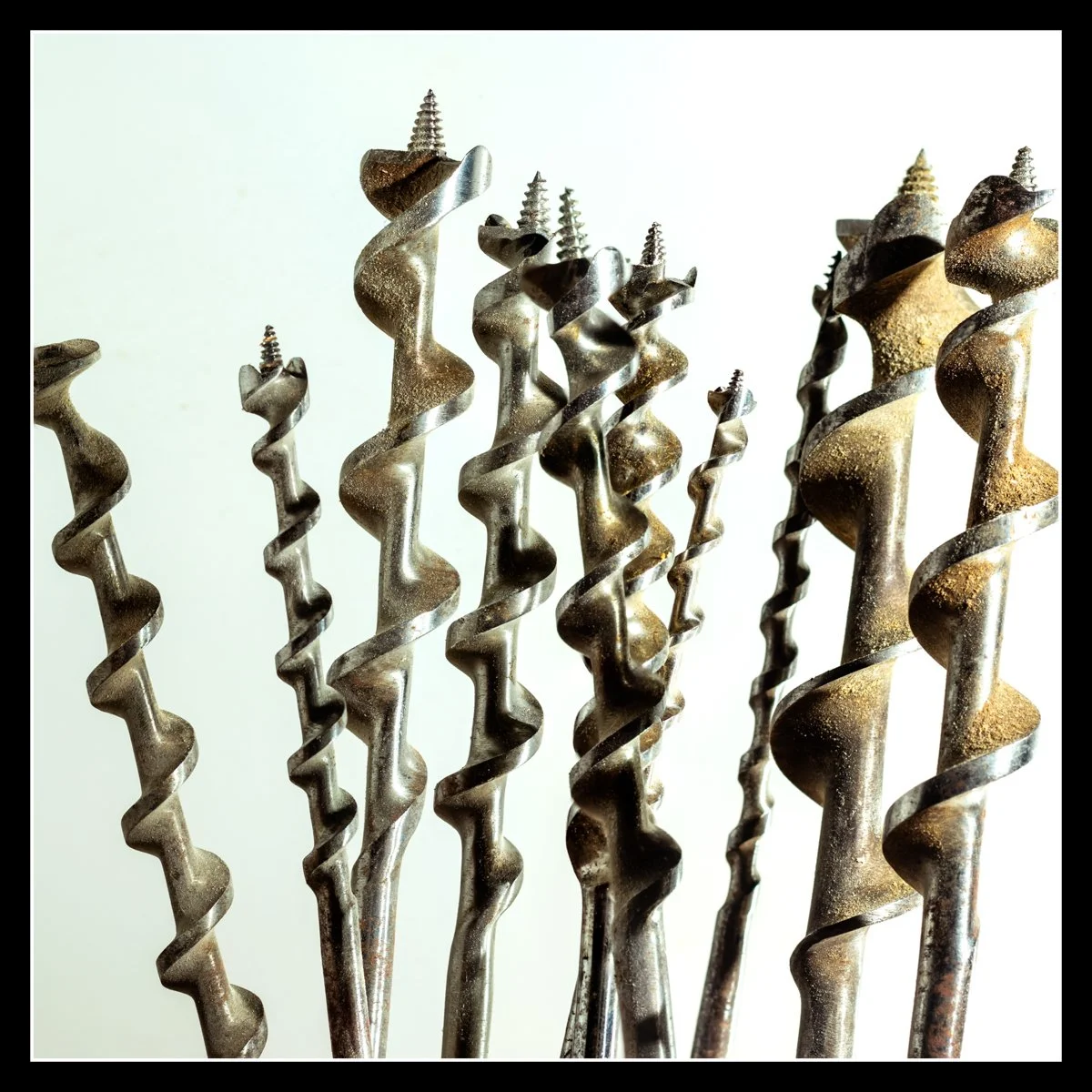 Auger bits standing upright on a white background, lit with side and back flashes to reveal spiral texture and dust.