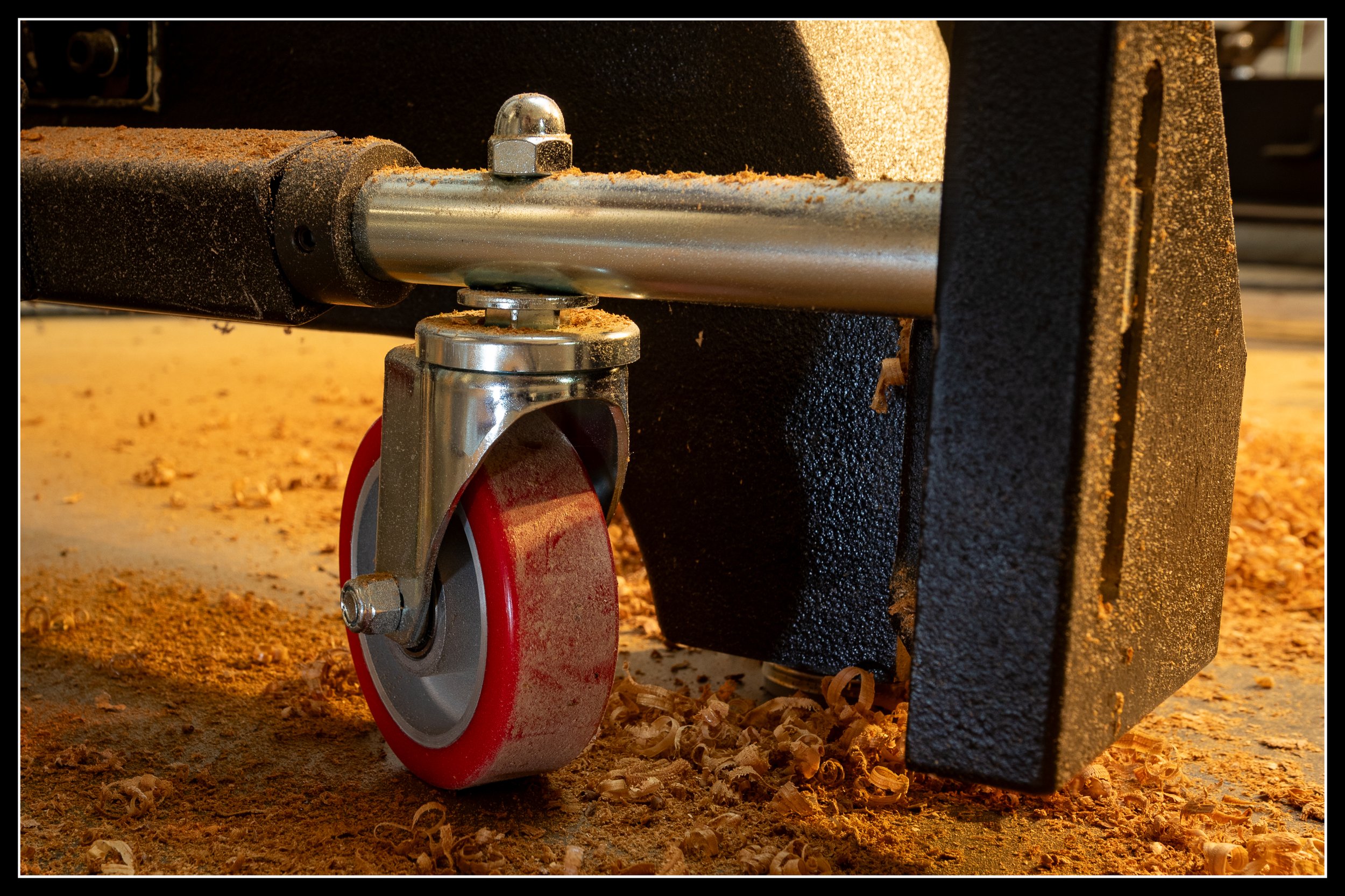 Caster wheel on the lathe’s mobile kit surrounded by fresh sawdust on the shop floor.