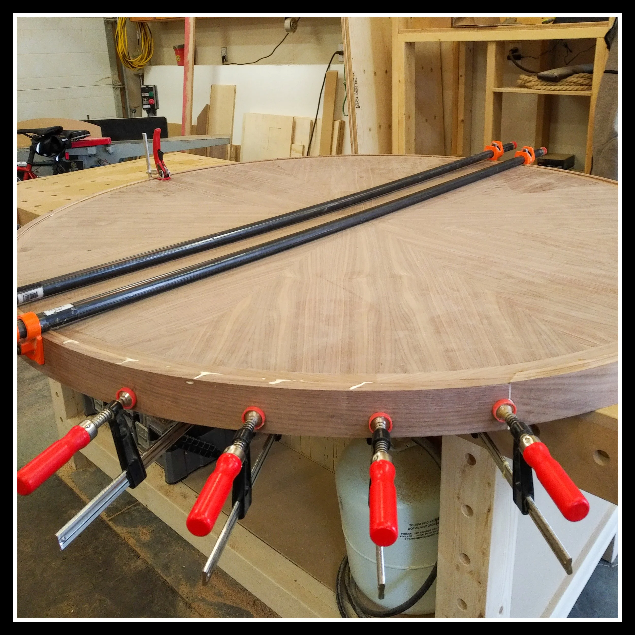 Bent lamination glue‑up for a circular table ring, with wet glue visible at the seams and multiple clamps applying pressure before profiling.