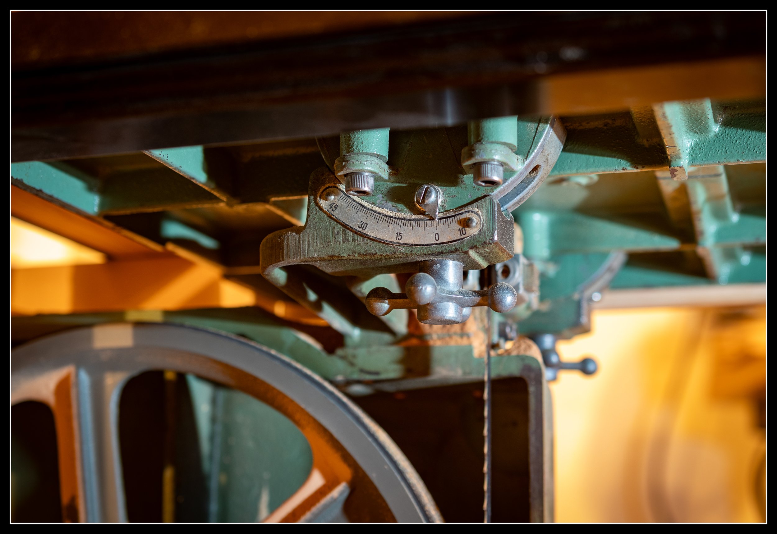 Close-up of the General 490 15-inch bandsaw’s cast‑iron trunnion and angle gauge assembly under the table, showing the heavy metal construction and precision adjustment hardware used in Canadian-made woodworking machinery.