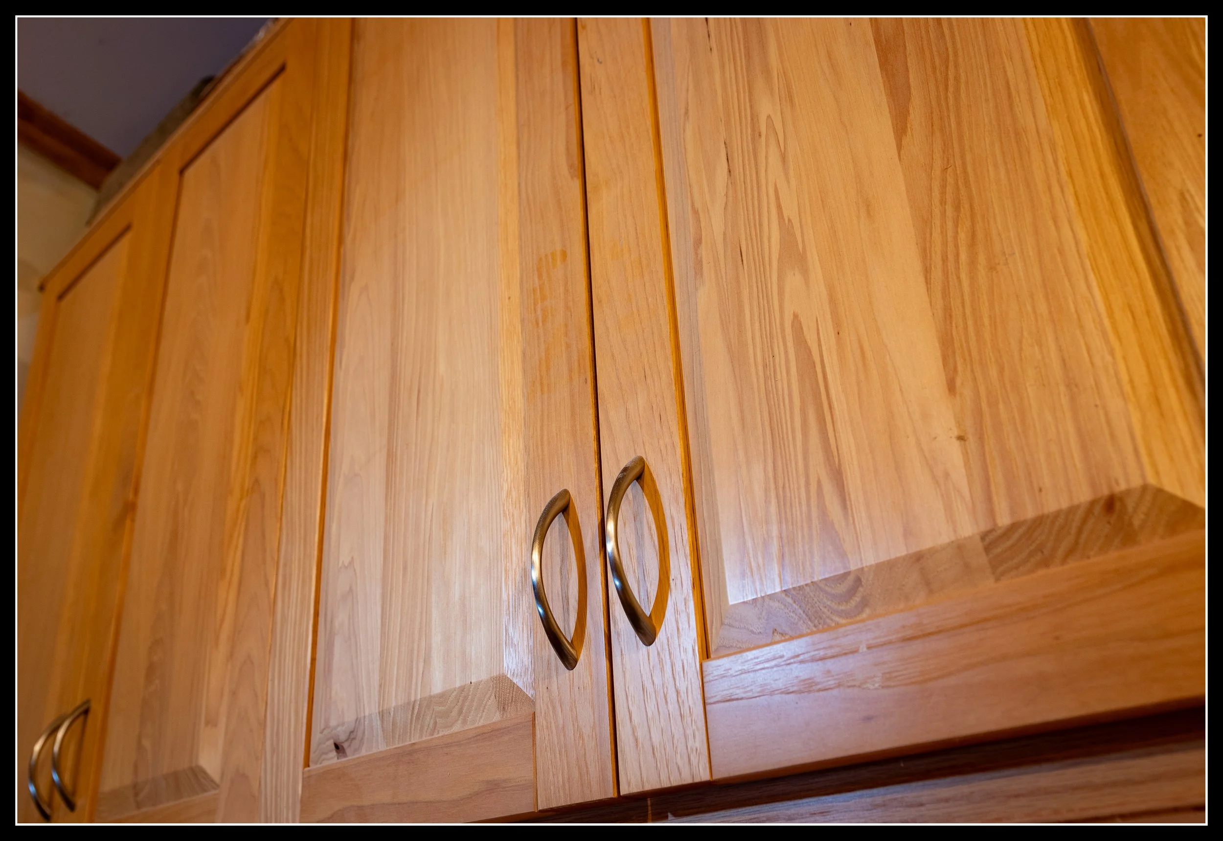 Raised‑panel hickory cabinet doors with natural grain variation, pale sapwood, darker streaks, and a clear water‑based polyurethane finish.