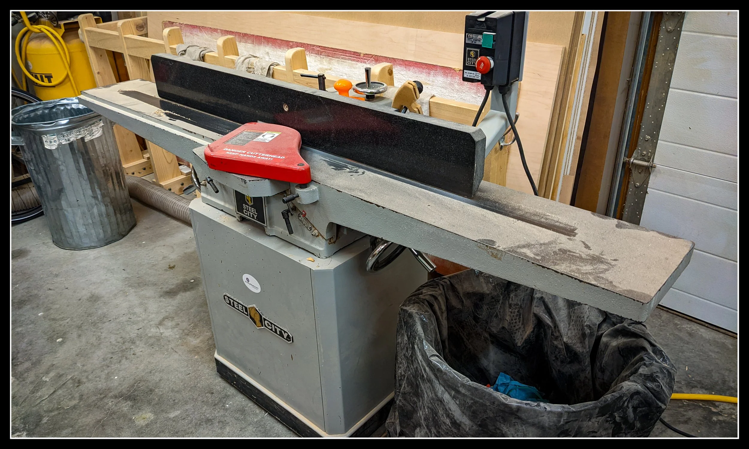 Steel City 8‑inch long‑bed jointer in a woodworking shop, showing fence, infeed and outfeed tables, red cutterhead guard, and upgraded carbide cutterhead; reliable mid‑range jointer used for flattening and straightening boards.