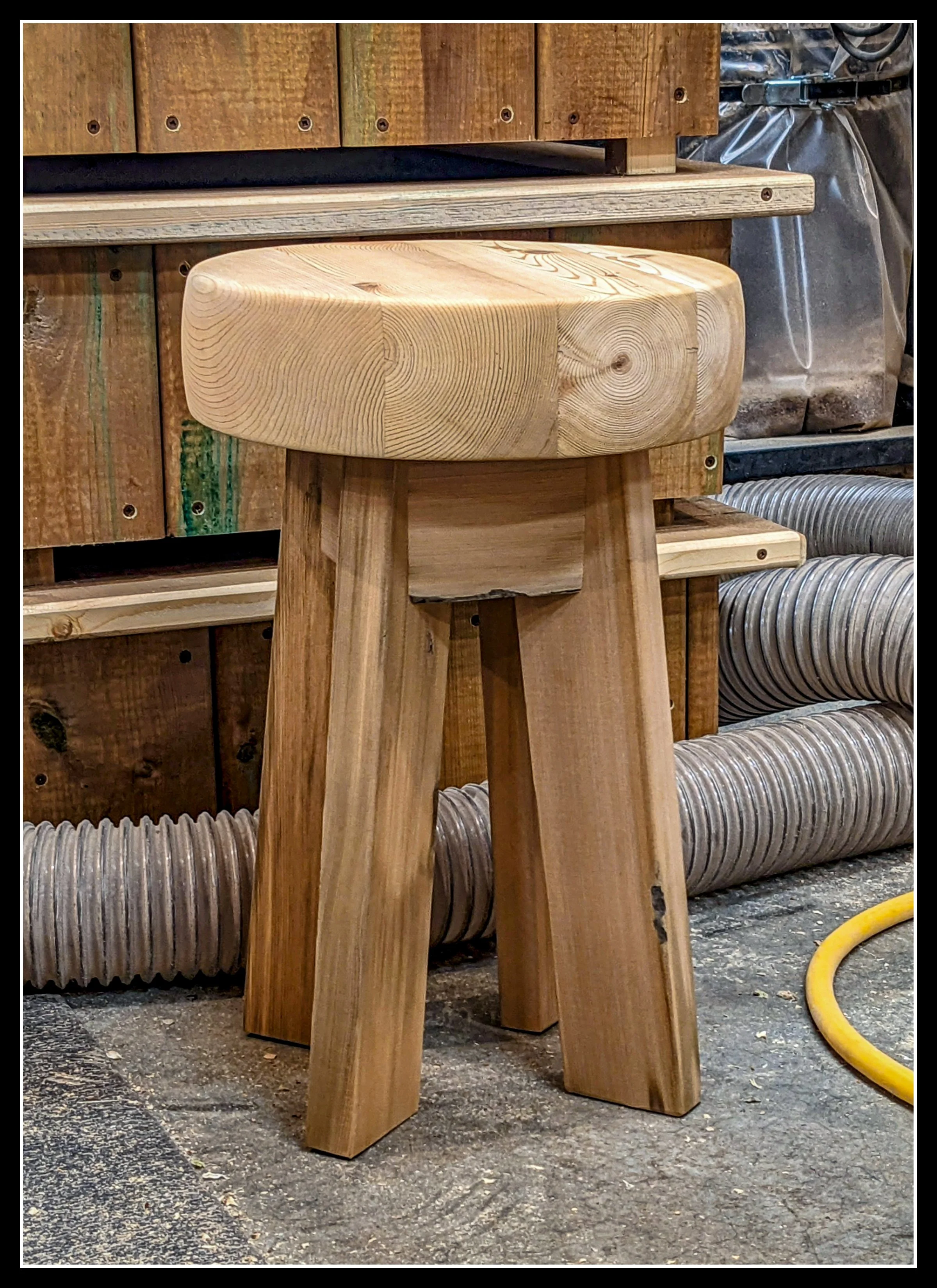 A wooden cedar stool with a thick, round seat and three legs in a woodworking shop.