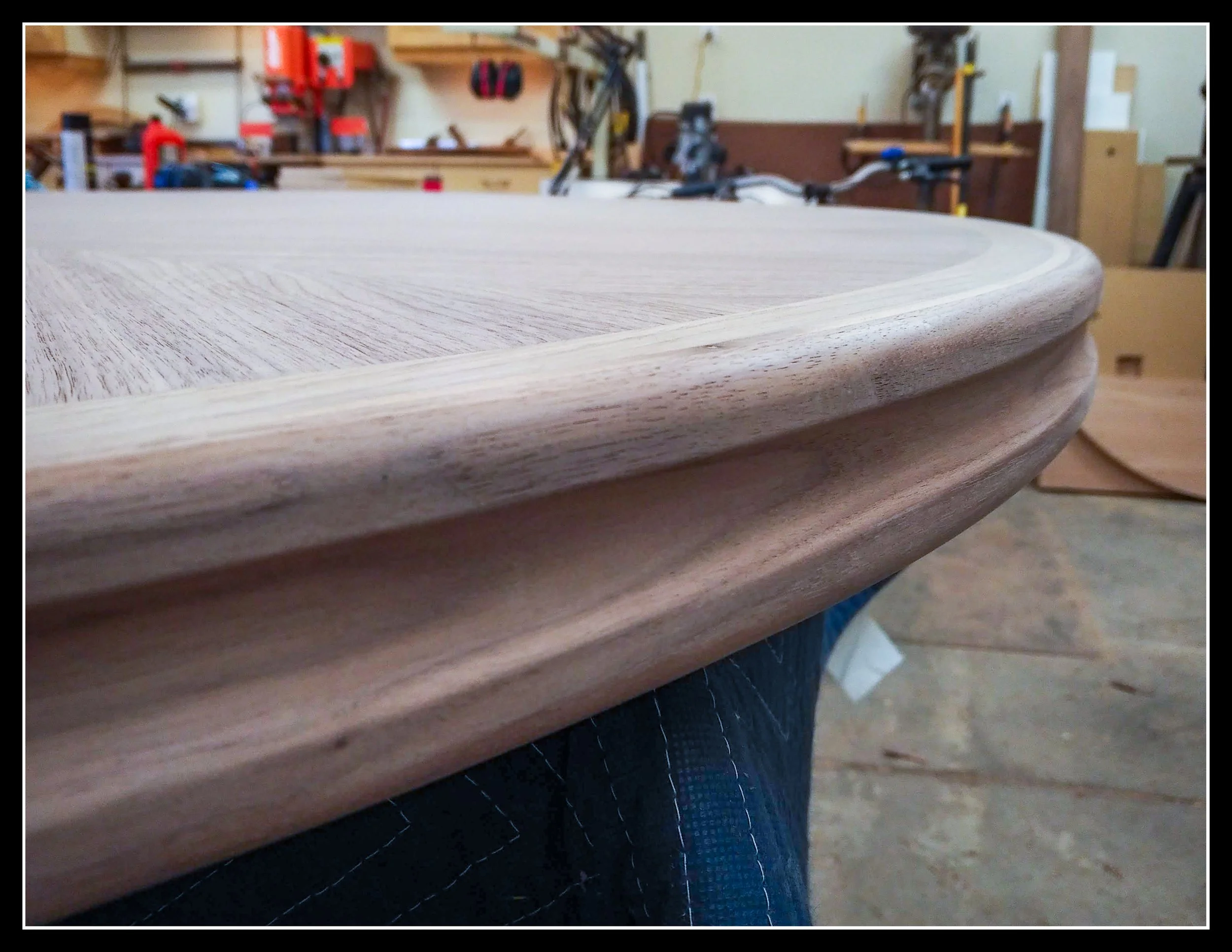 Rounded walnut table edge profile with smooth layered contour in a woodworking shop.
