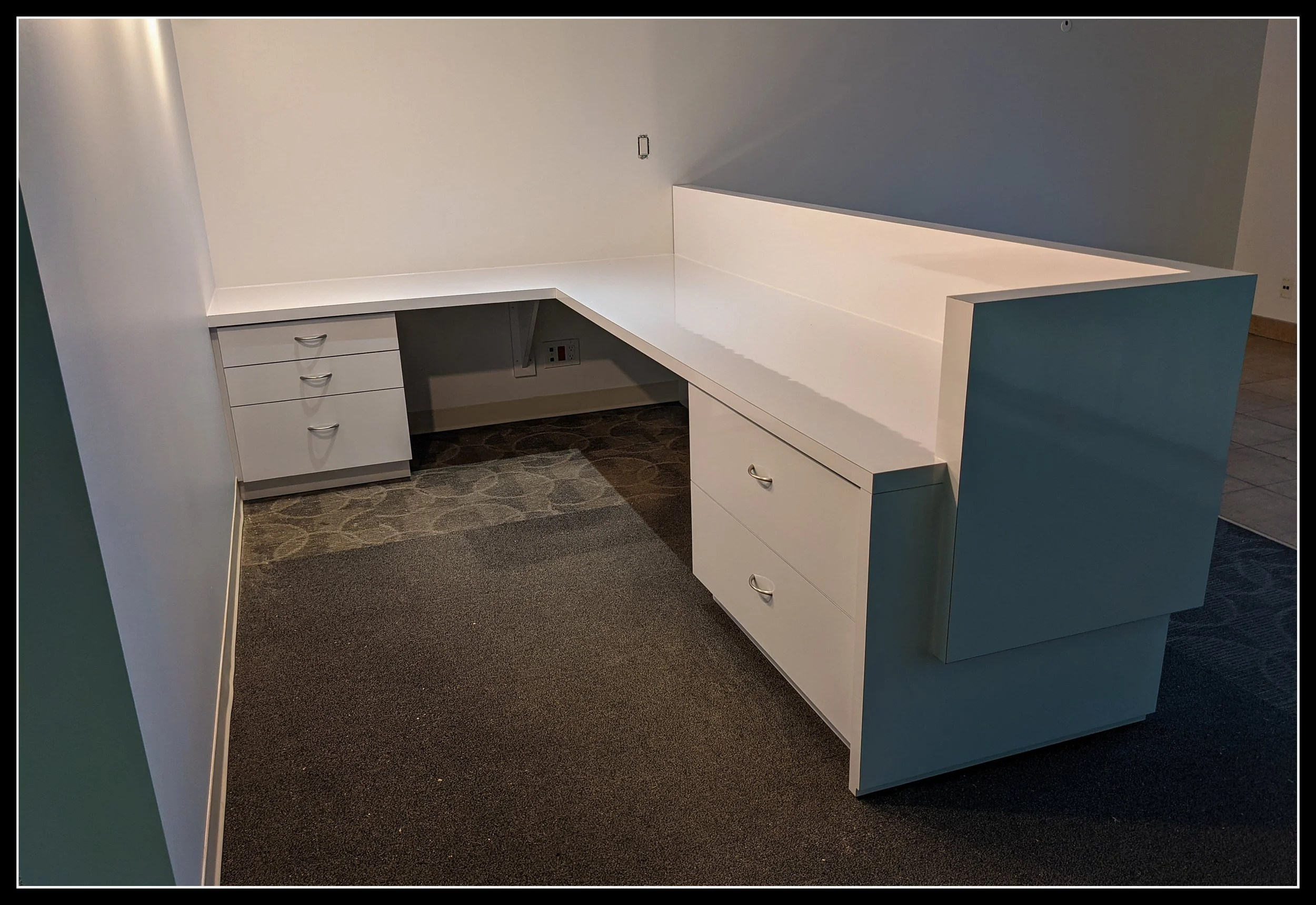Gloss‑white laminate reception desk in a realtor’s office with modern cabinetry, drawers, and a raised counter designed for daily commercial use.