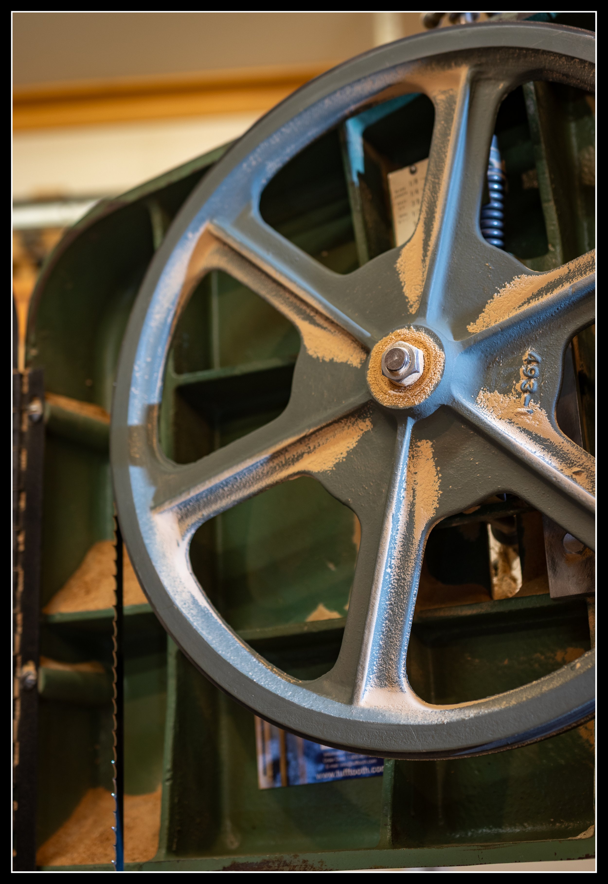Close-up of the General 490 15-inch bandsaw’s cast‑iron upper wheel assembly, showing the heavy spokes, hub, and frame construction that keep the blade stable and tracking true in a woodworking shop.