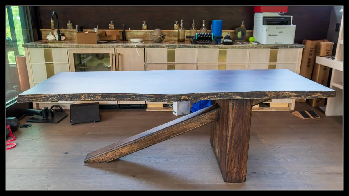 A modern wooden dining table with a thick, polished top and distinctive angled legs in a contemporary kitchen.