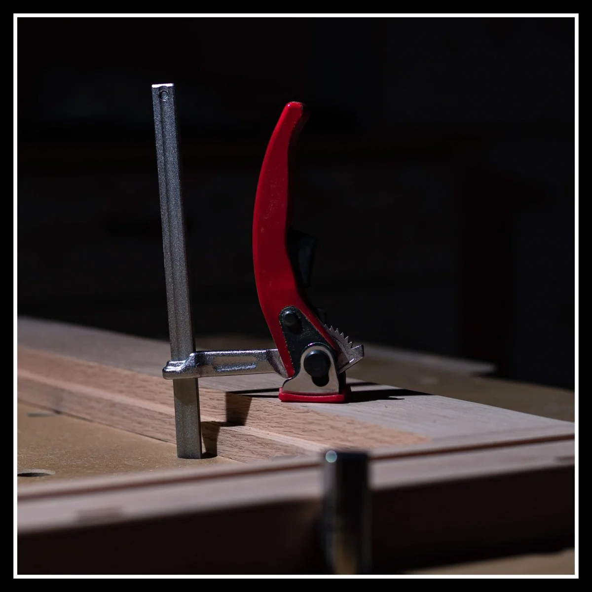Surface clamp securing a rift‑cut red oak board to a workbench for milling, showing close-up detail of the clamp mechanism and wood grain.