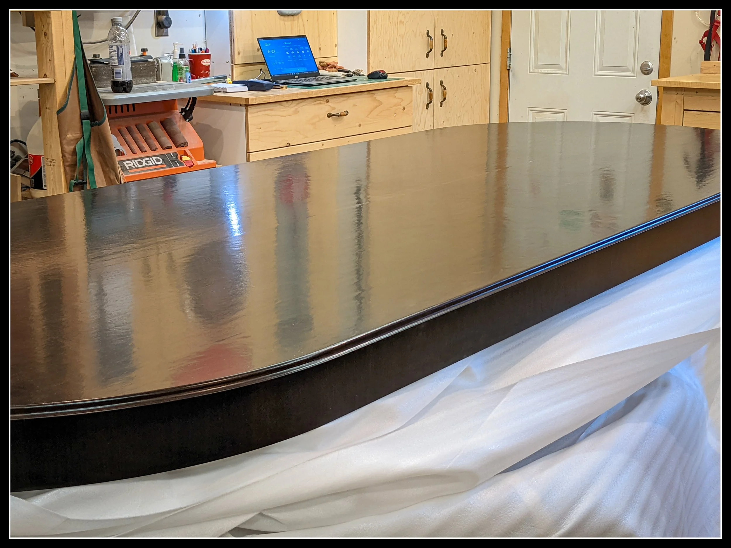 Freshly stained and finished 12‑foot solid walnut oval table top in woodworking shop, ready for delivery.