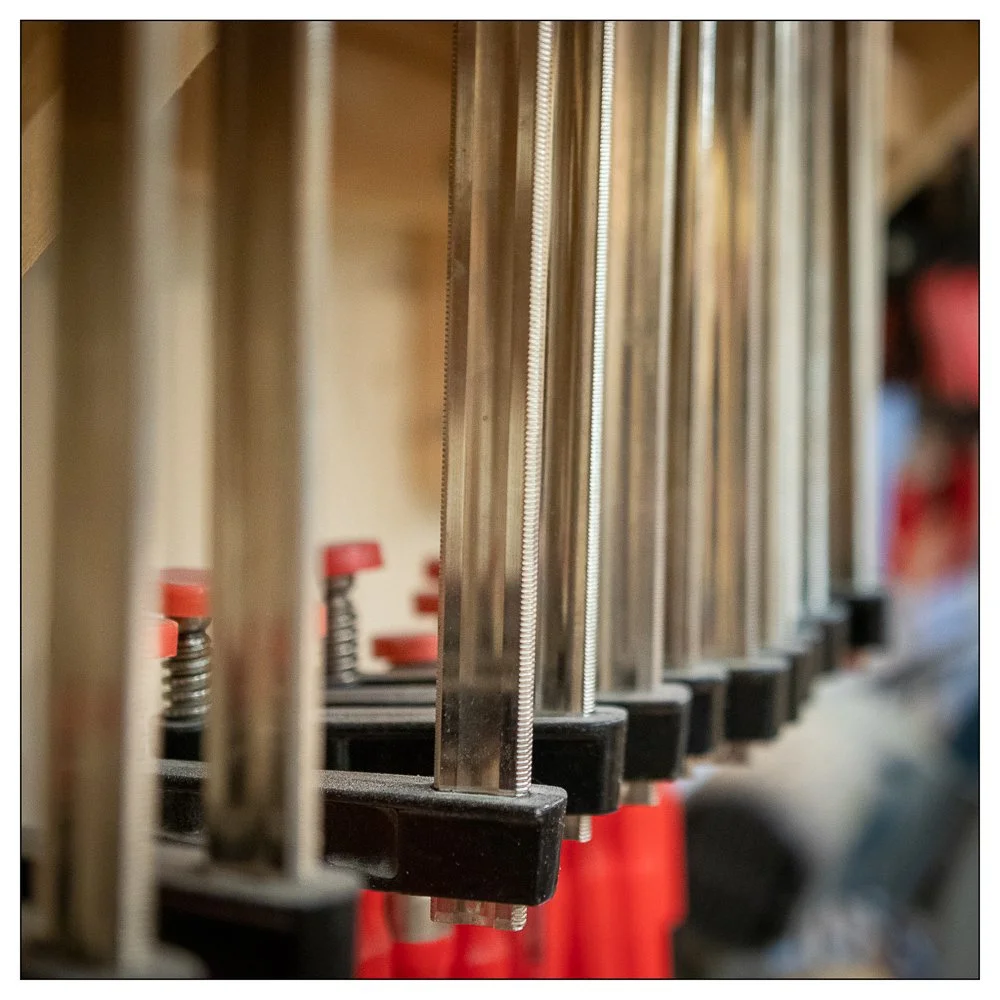 Benchmark bar clamps hanging in a woodworking shop, showing chrome I‑beam bars that resist glue and prevent bending.