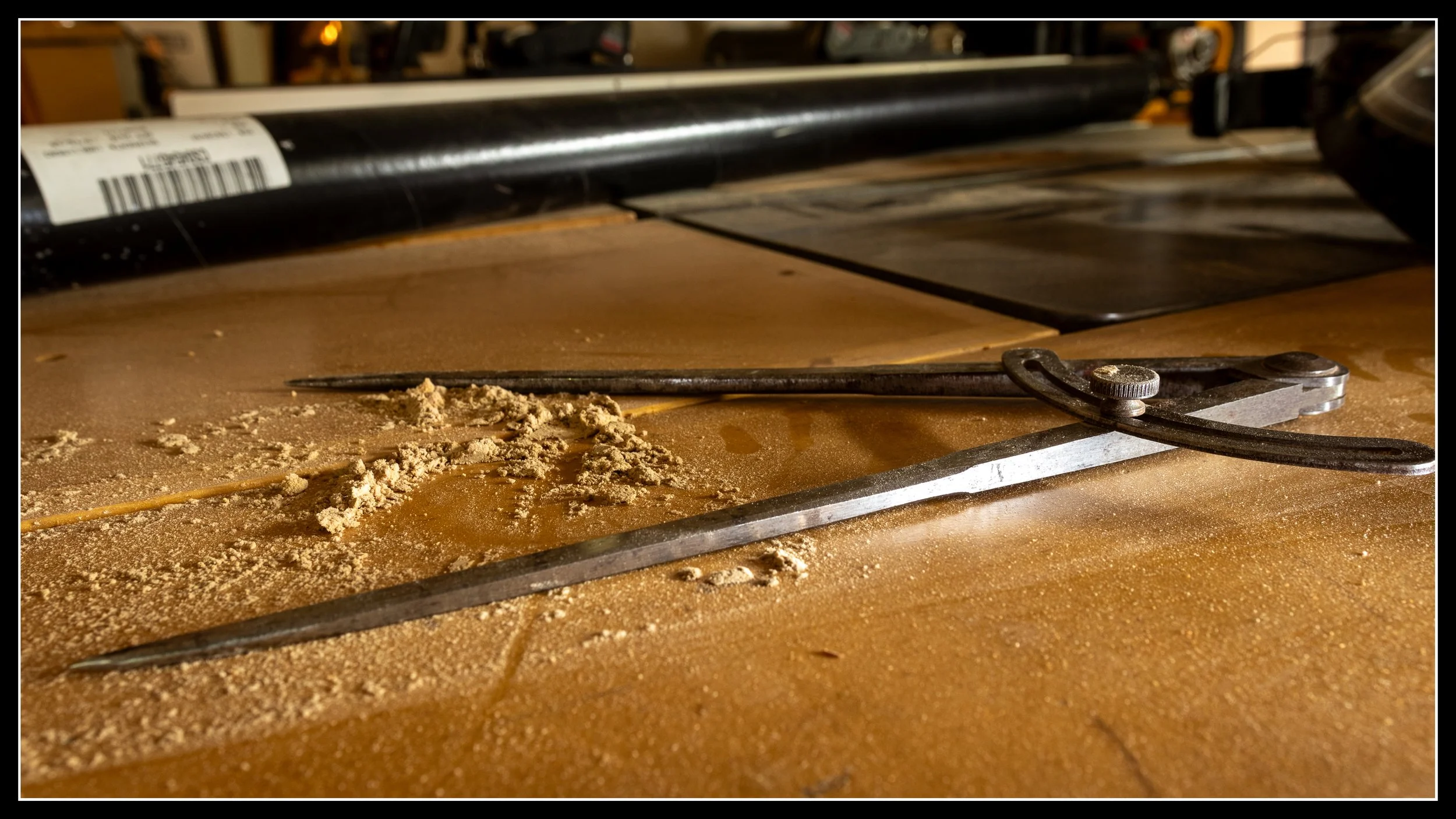 A pair of metal dividers resting quietly on a woodworking bench, a small moment from the quieter side of shop life.