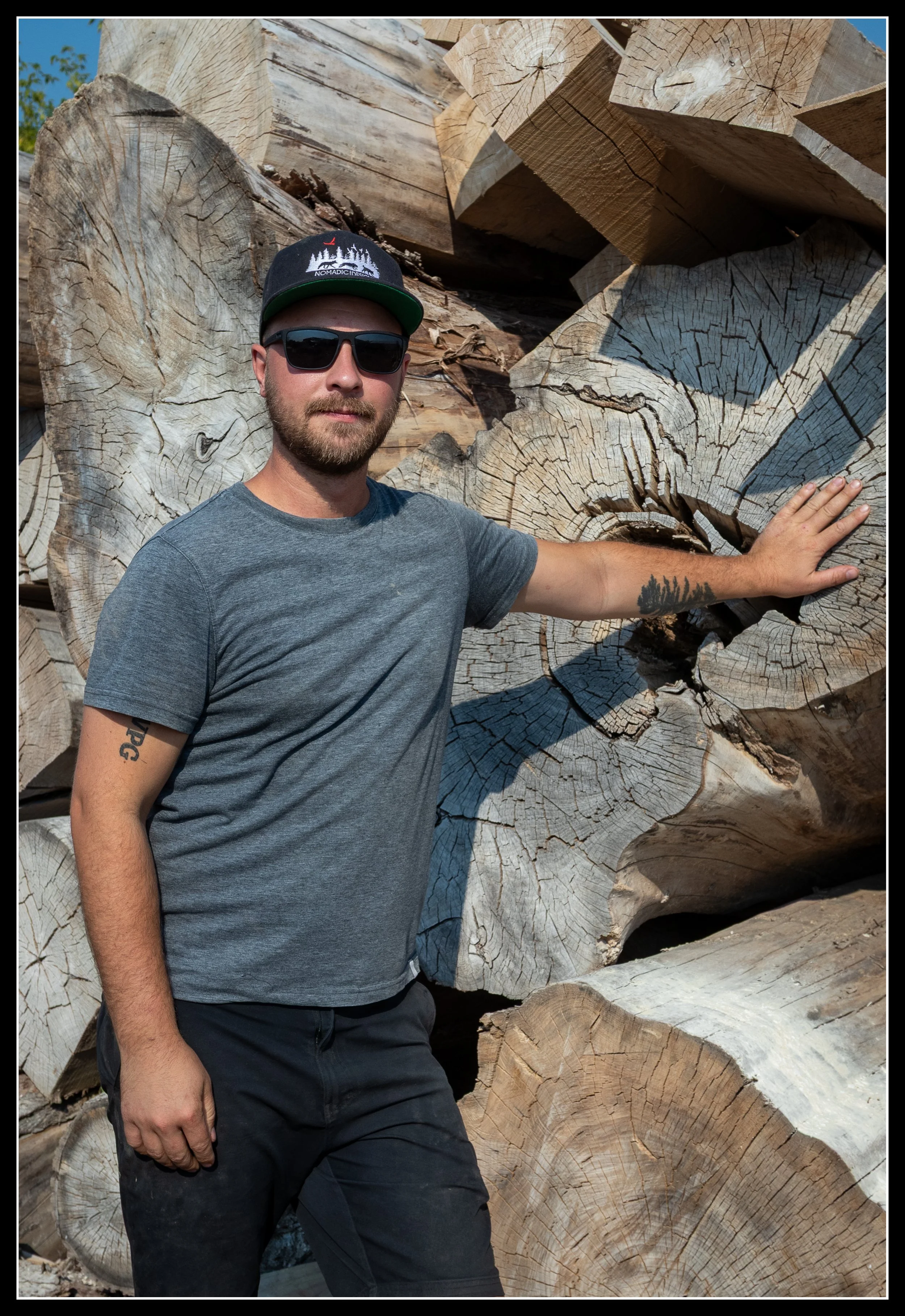 Mike McGary standing beside large elm logs, co‑owner of the mill that makes elm lumber available to woodworkers.