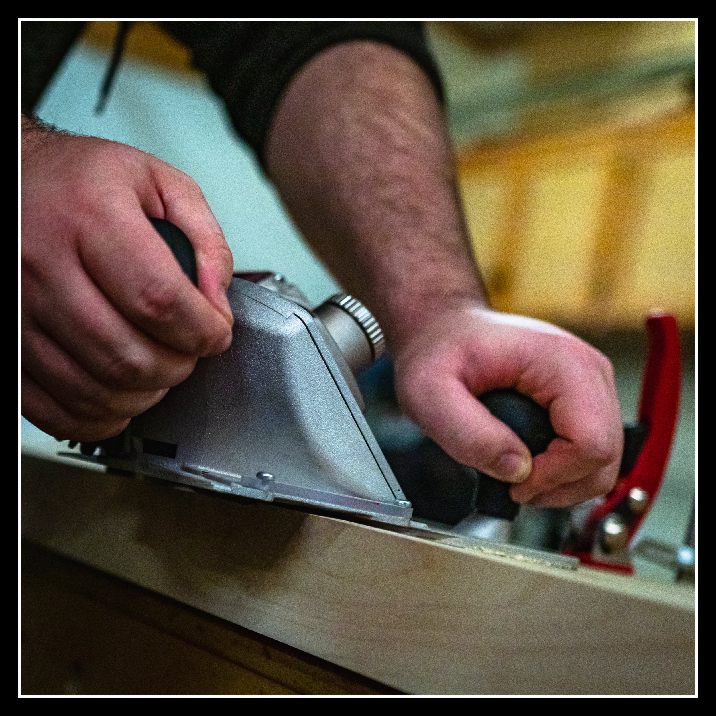 Hands guiding a lipping planer along the edge of a board, trimming it slowly and precisely as a symbol of steady recovery in the woodworking shop.